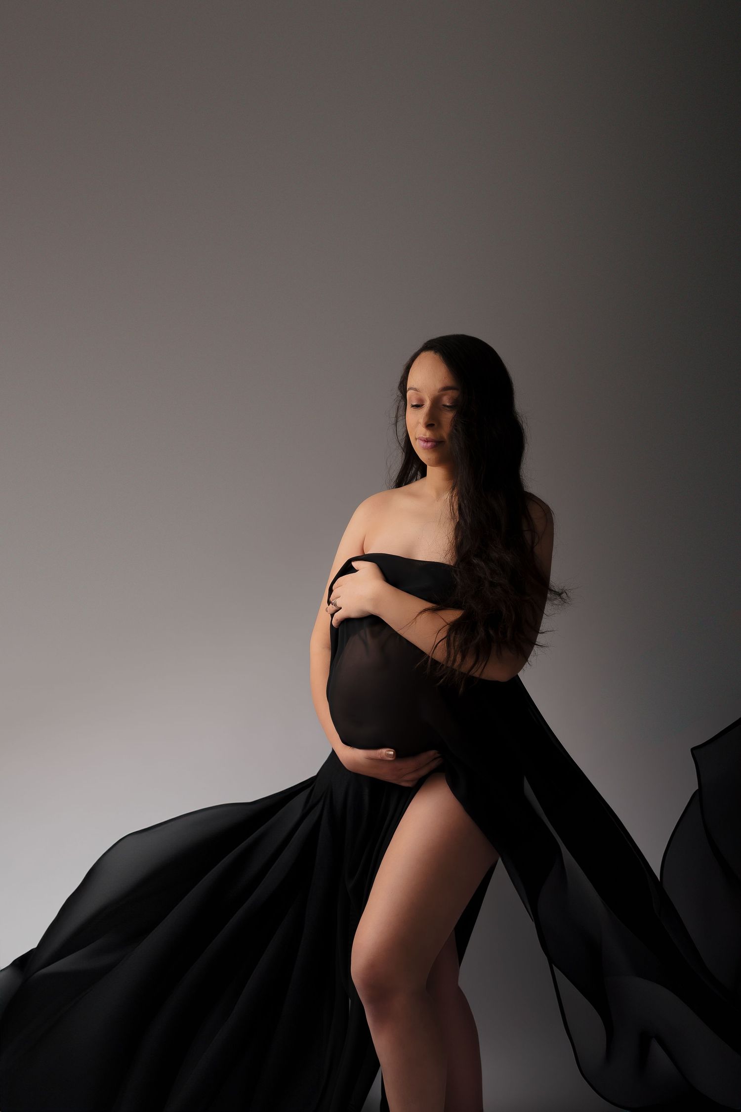 Dramatic maternity portrait with flowing black fabric against grey background.