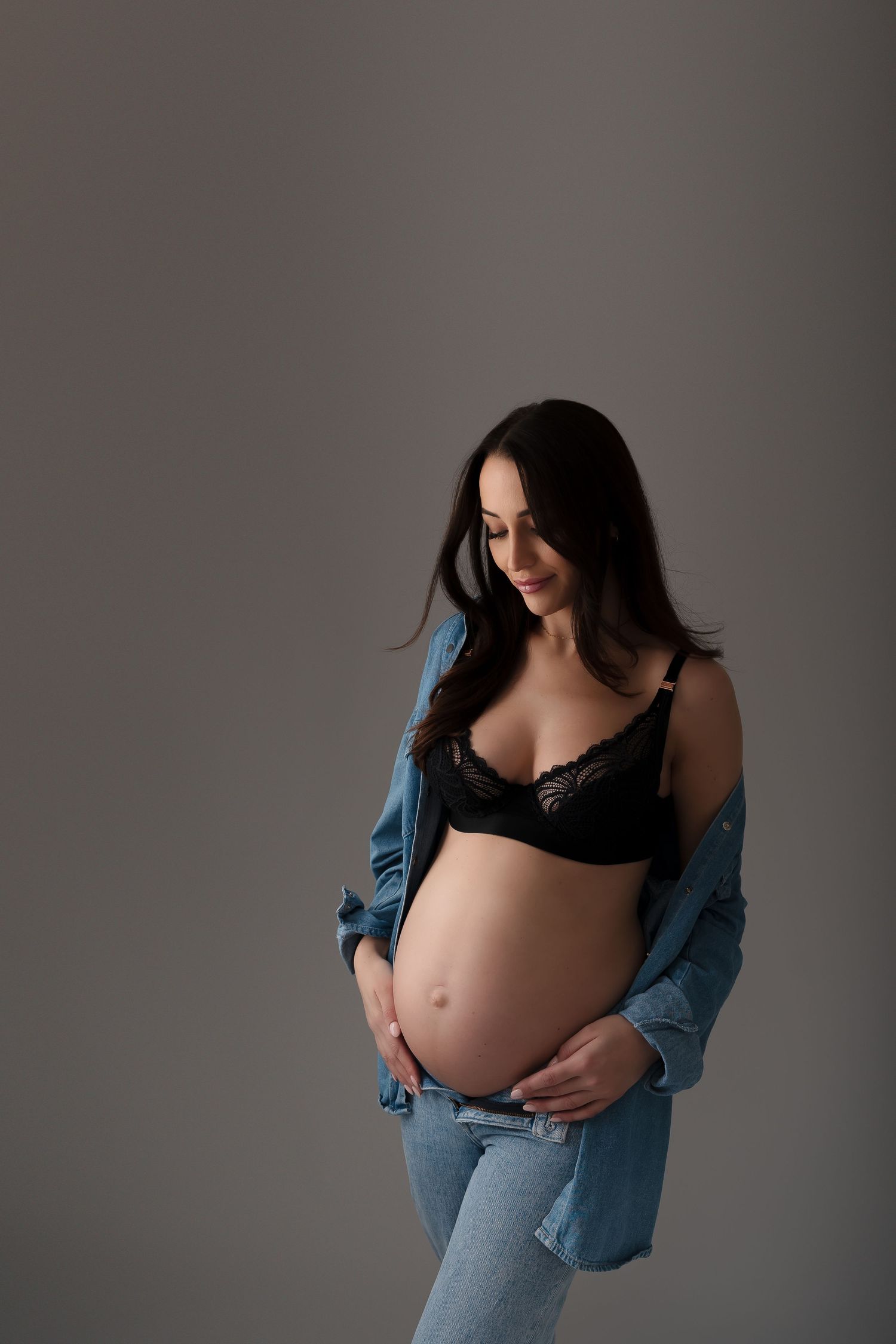 Casual maternity photo in denim and black lingerie against grey background.