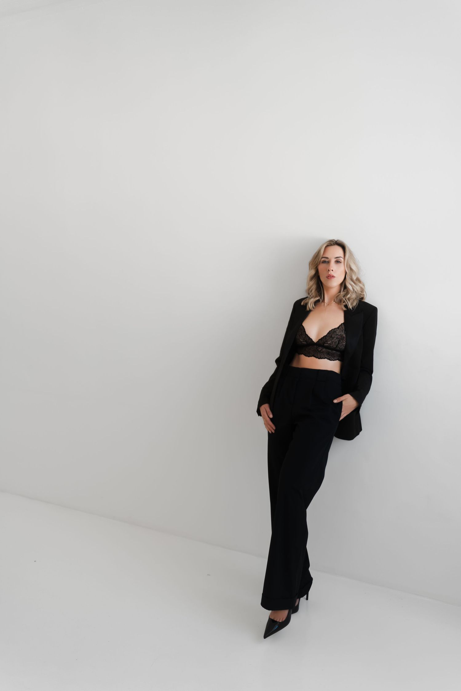 Model in all black ensemble poses elegantly against minimalist white studio background.