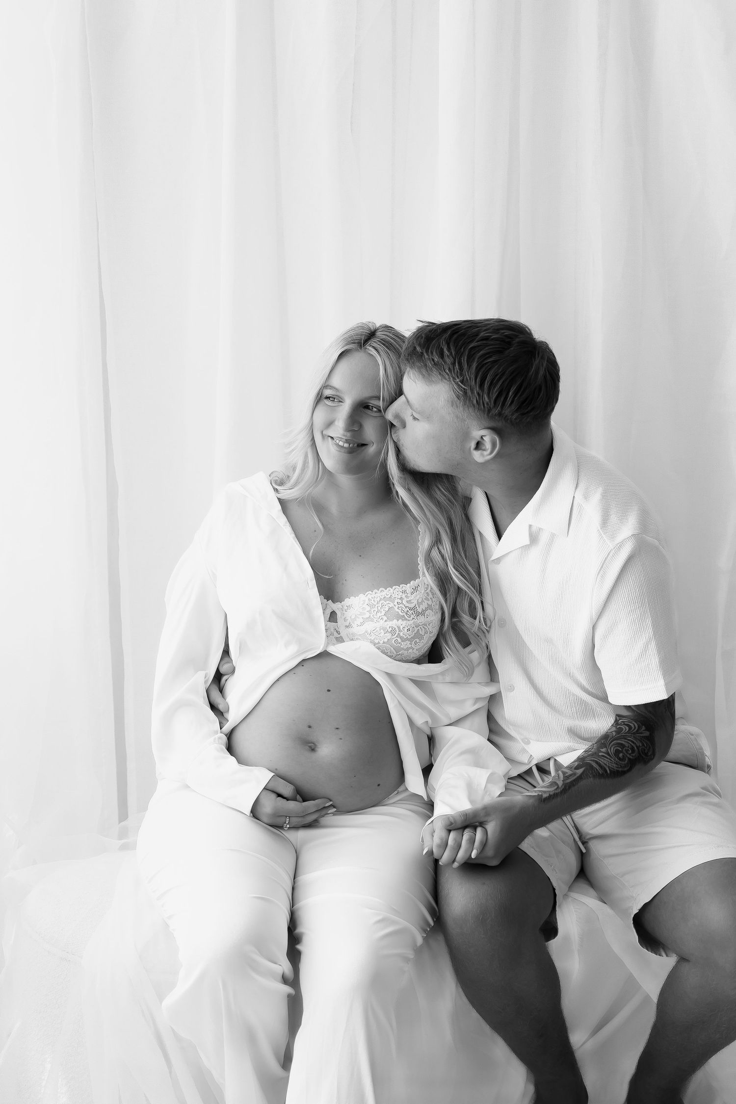 Romantic black and white maternity photos of couple in white clothing sharing tender moments.