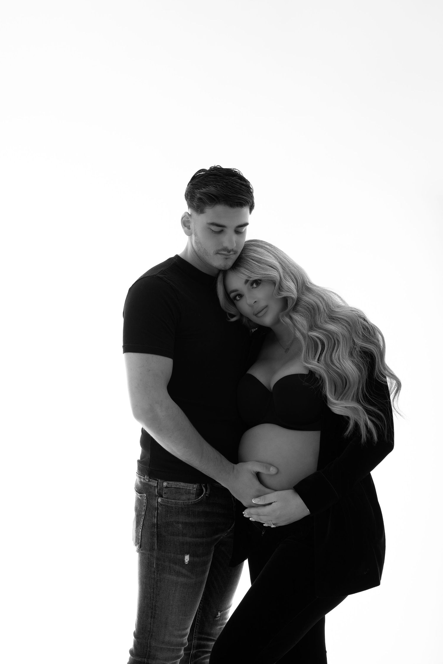 Black and white maternity photos showing couple embracing against white background.