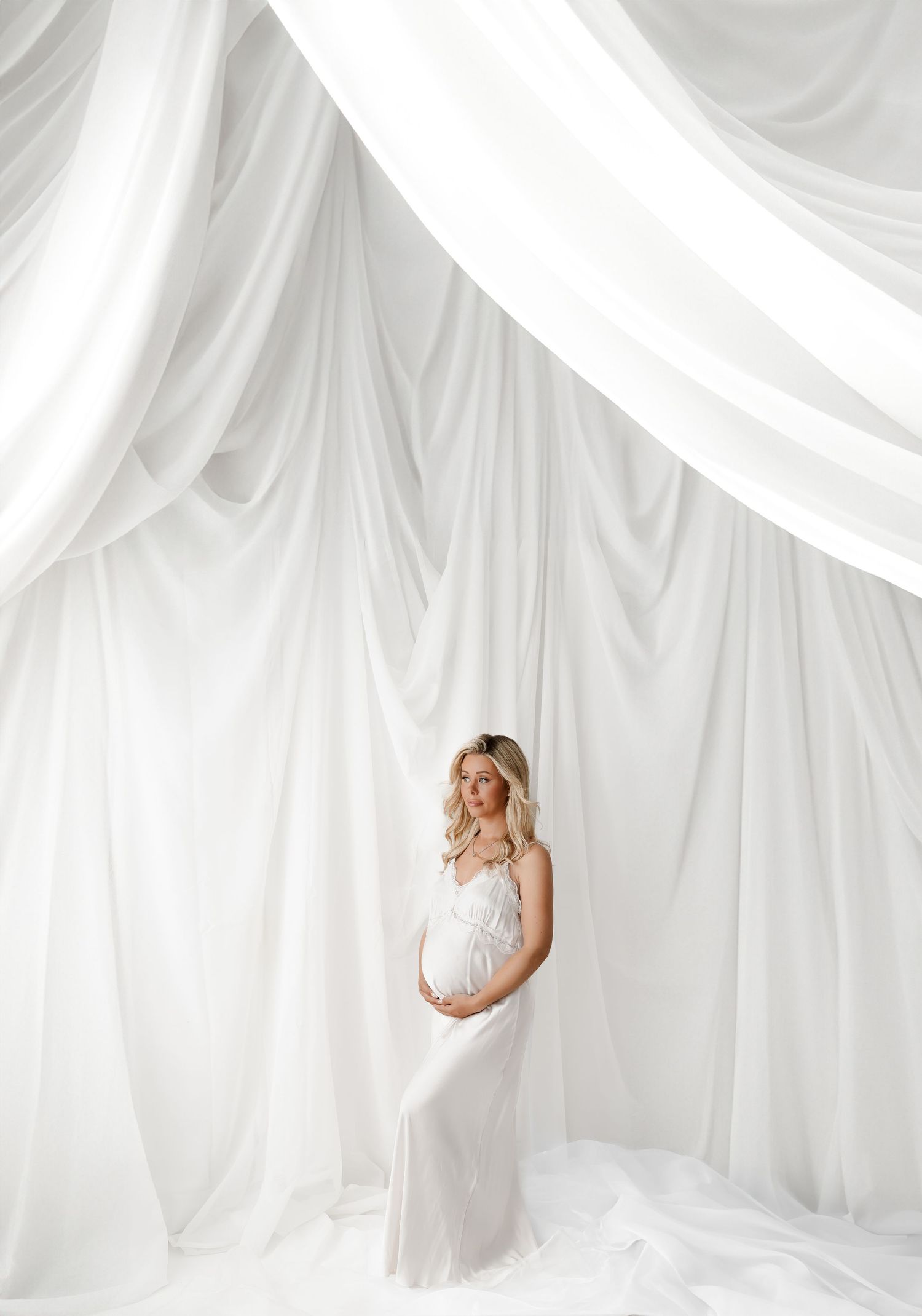 Ethereal maternity photos with flowing white fabric and soft lighting.