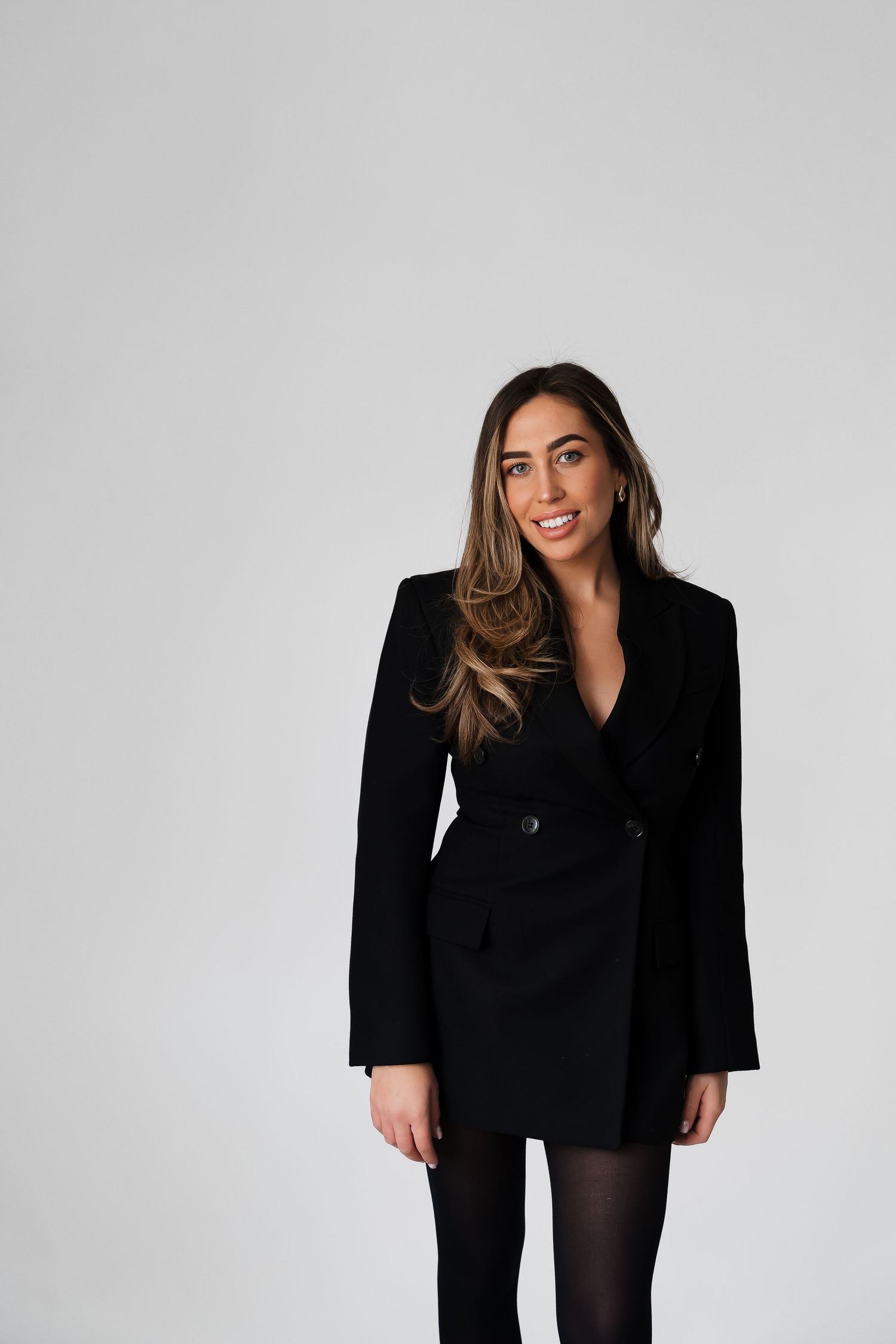 Stylish woman wearing black blazer dress poses against white background.