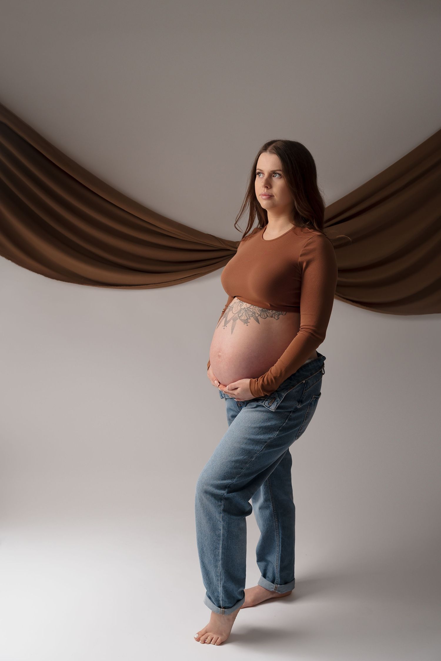Natural maternity portrait with brown backdrop and casual clothing.