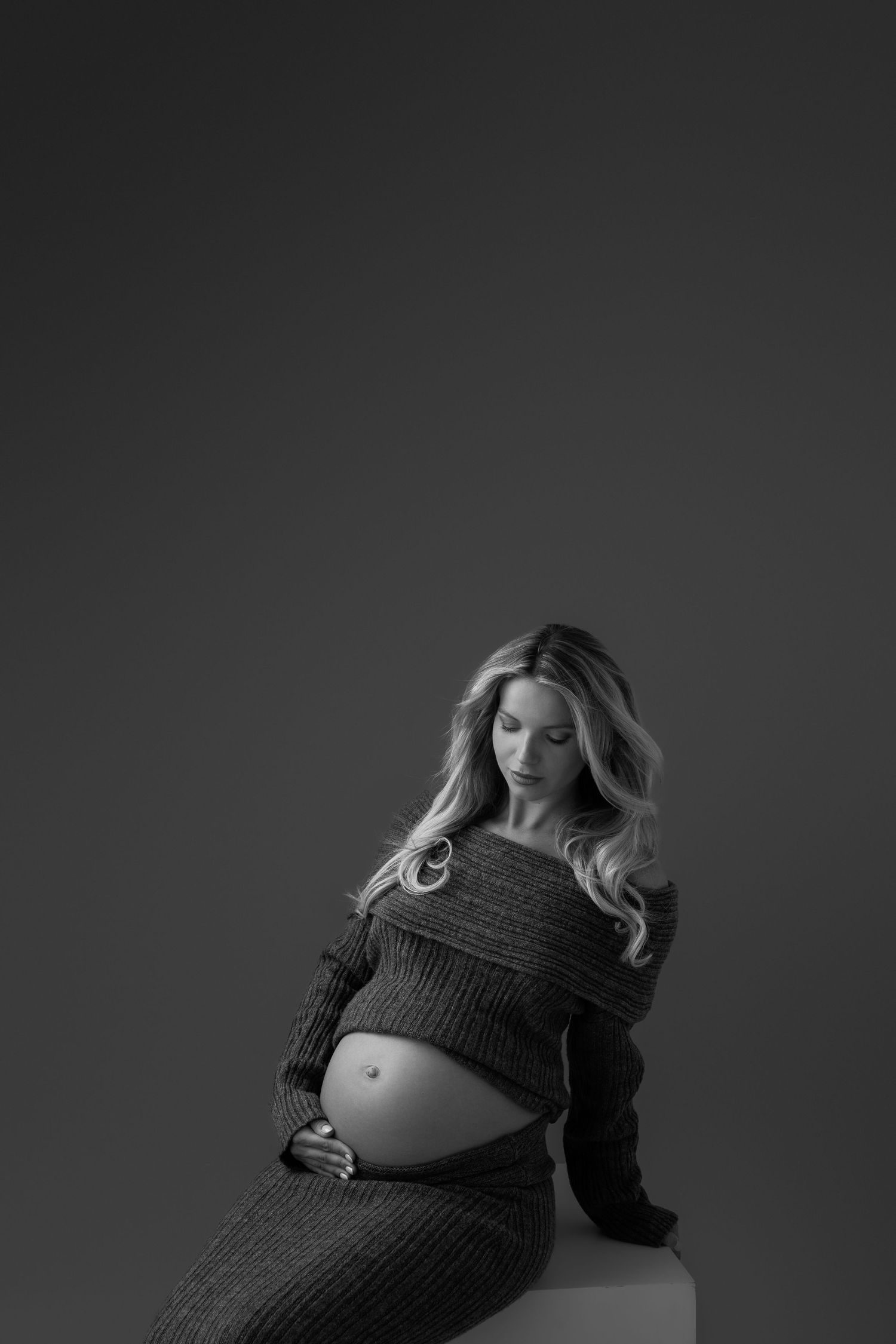 Moody black and white maternity portraits in knit dress against dark background.