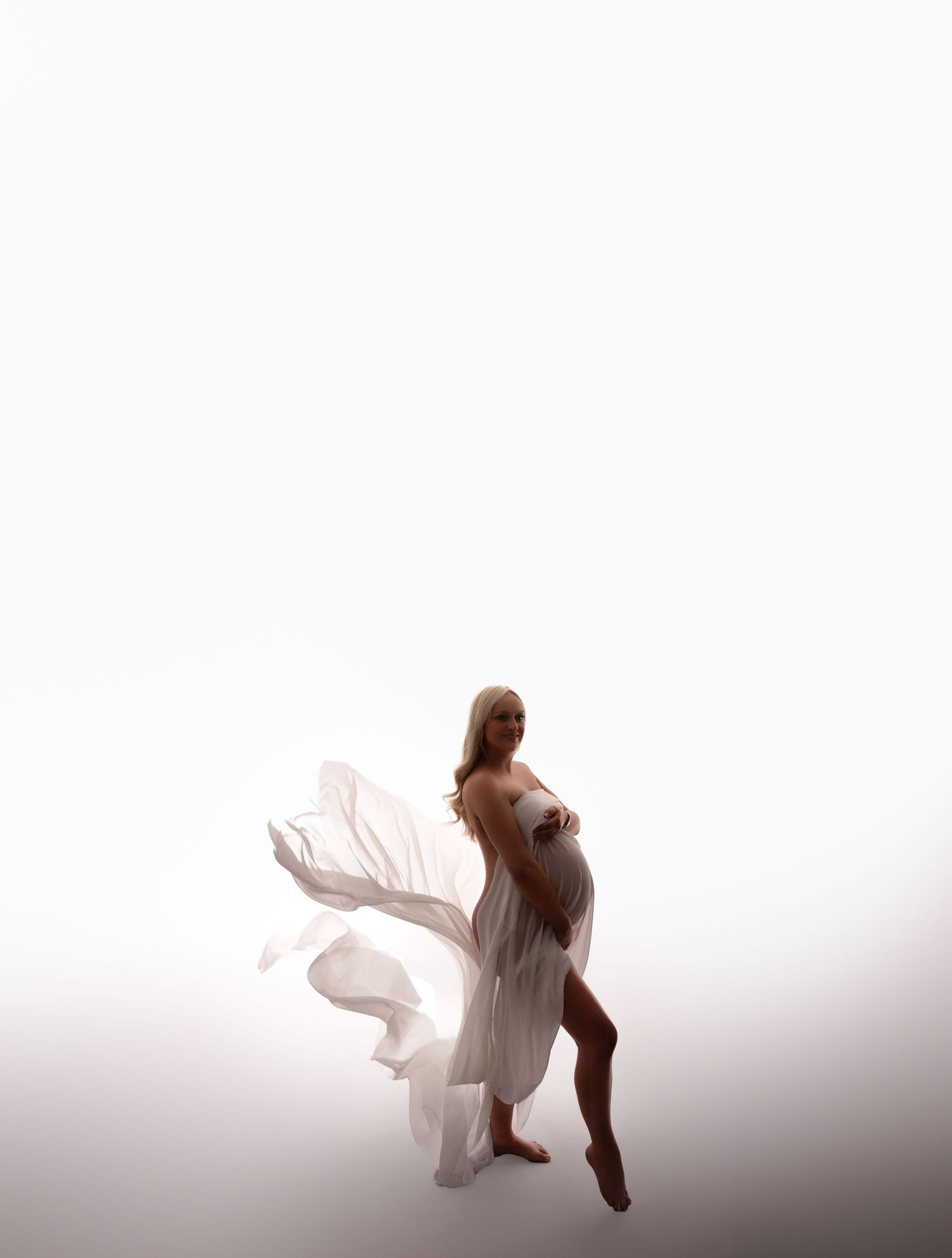 Minimalist maternity silhouette with billowing white fabric against light background.