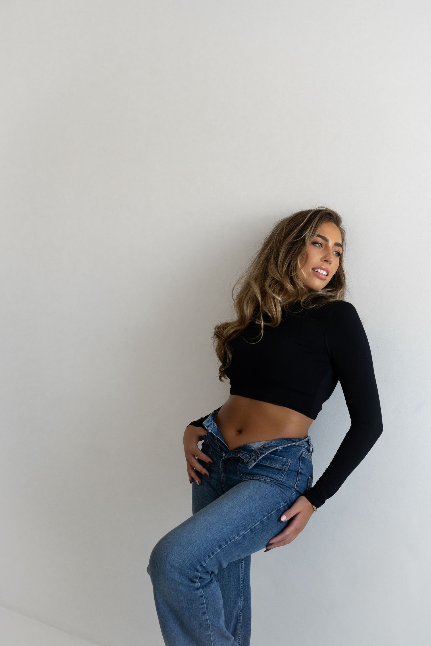 Fashion model poses in black crop top and blue jeans against white background in dynamic poses.