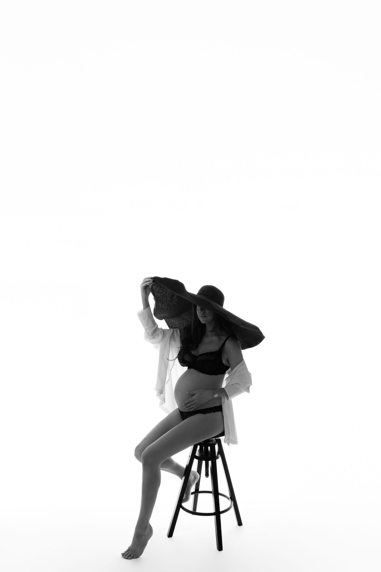 Artistic black and white photo of person posing on stool in studio setting.