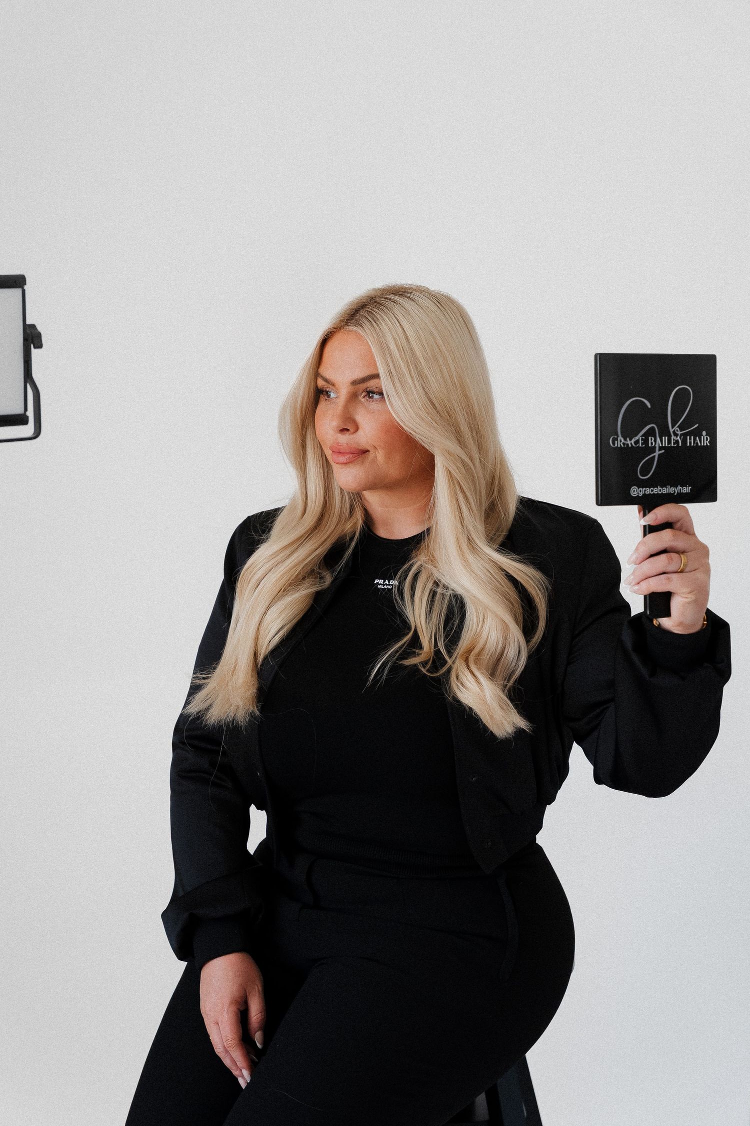 Blonde woman in black outfit holding a dark book in a professional photo studio setting.
