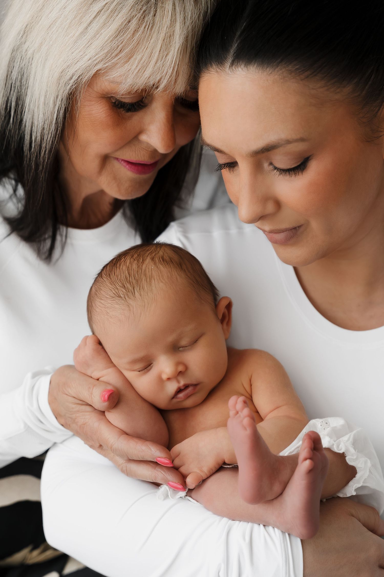 Three generations share tender moment with sleeping newborn baby.