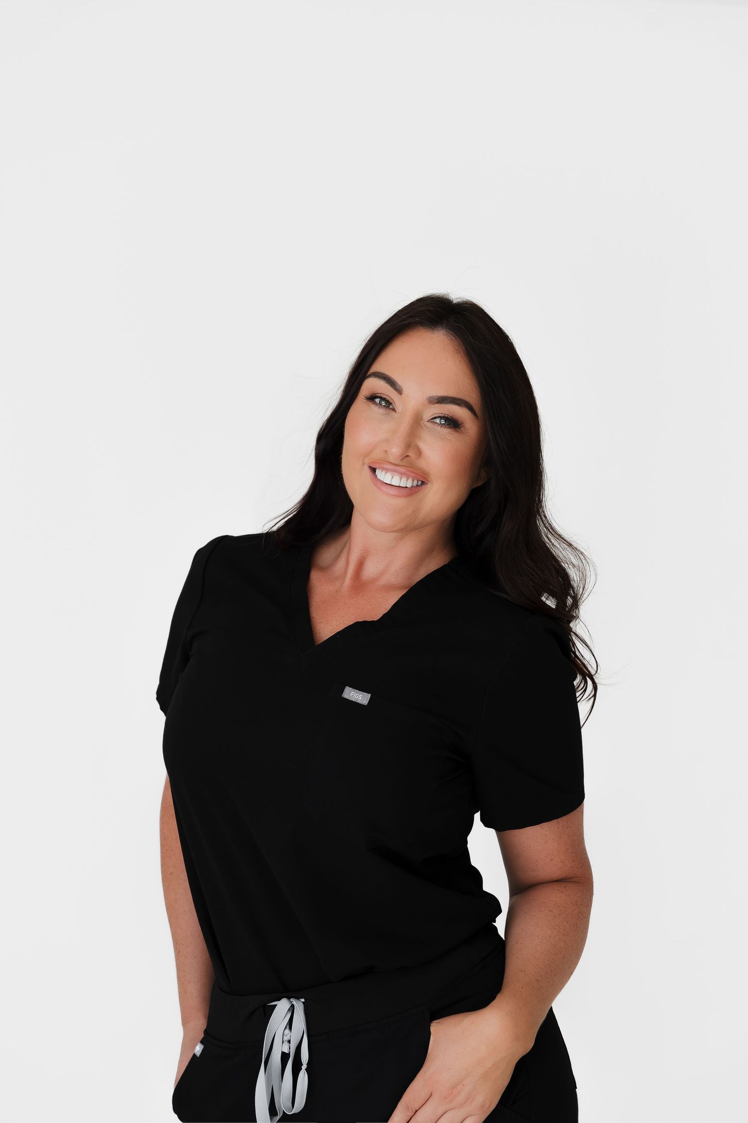 Woman in black medical scrubs top smiling against white background, professional healthcare uniform.