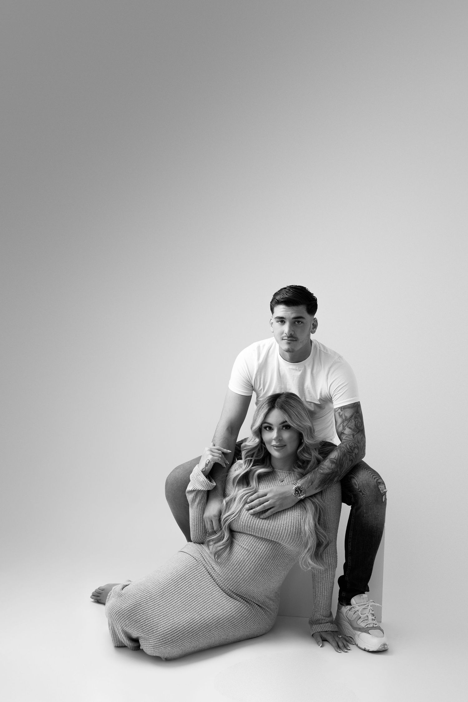 Black and white maternity photo of couple in casual wear sitting together.