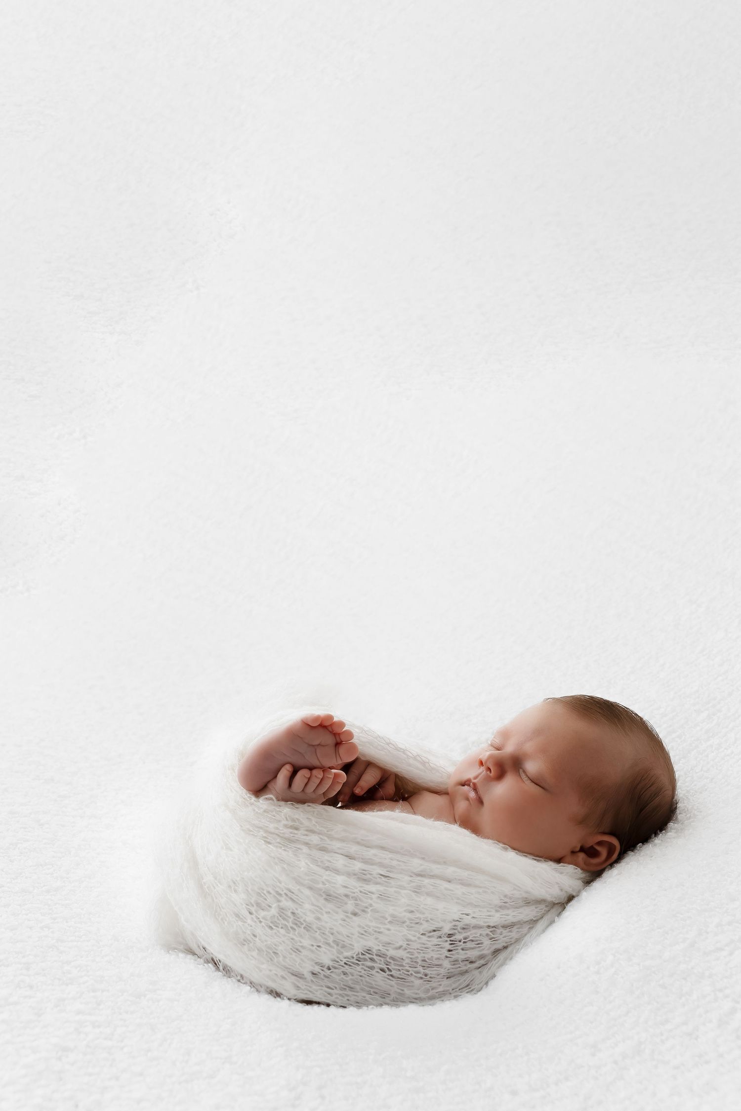Peaceful newborn baby sleeping in white swaddle wrap against white background.