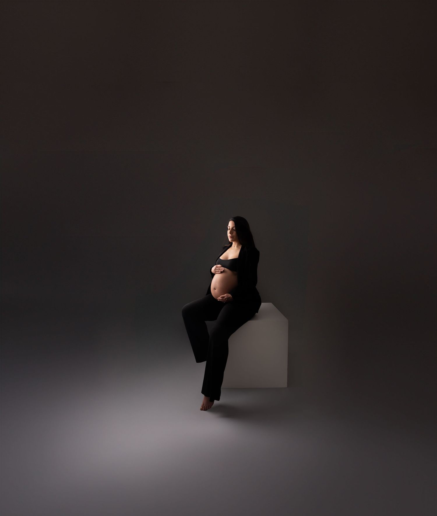Dramatic low-key maternity portraits with artistic lighting and dark background.