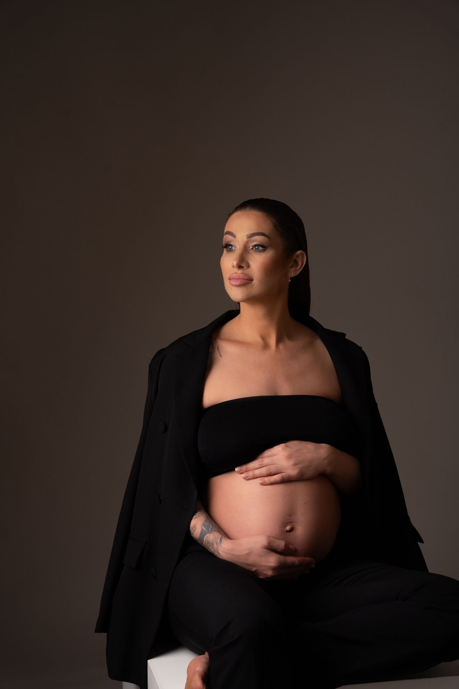Modern maternity portrait with woman in black outfit against dark background.