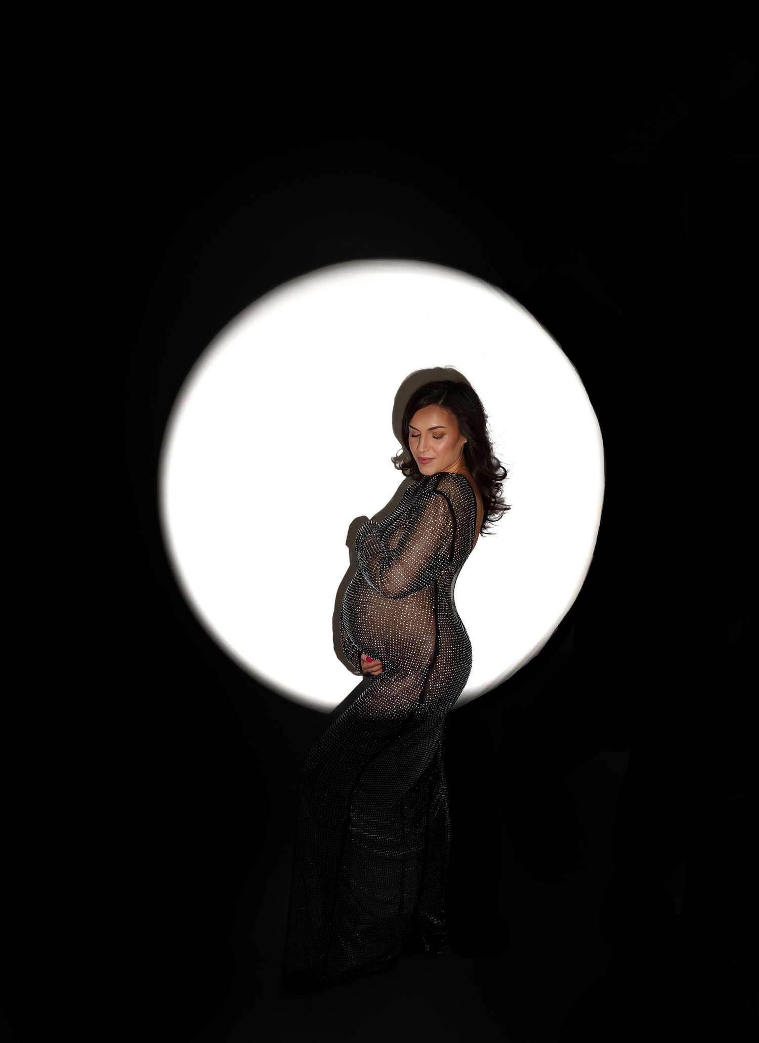 Dramatic maternity silhouette with a glowing white circular backdrop behind the expectant mother.