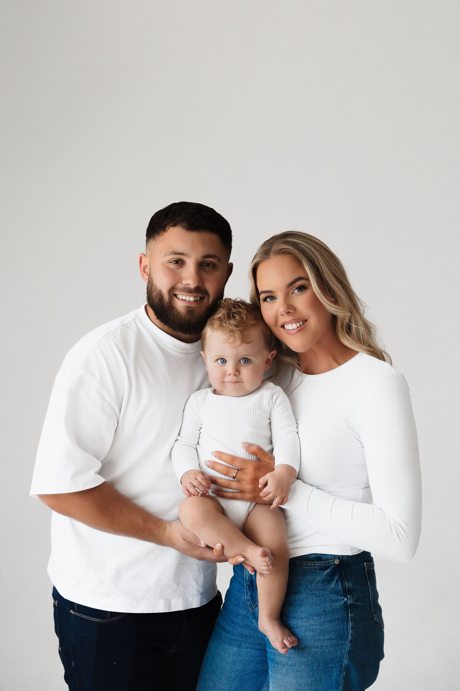 Family in coordinating white and denim outfits poses together against white background.