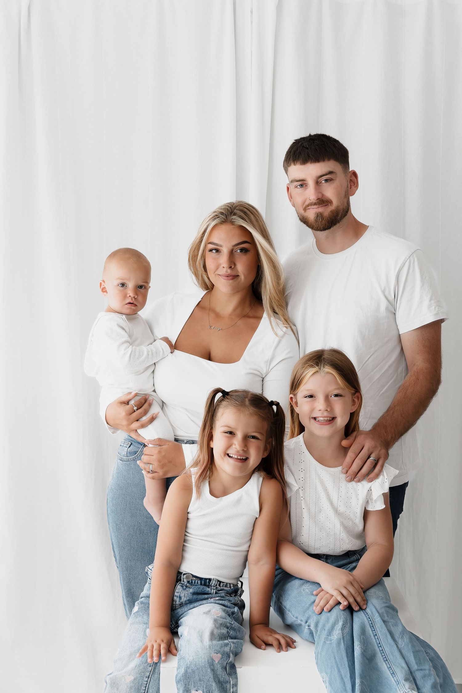 Family portrait with parents and three children against white backdrop.
