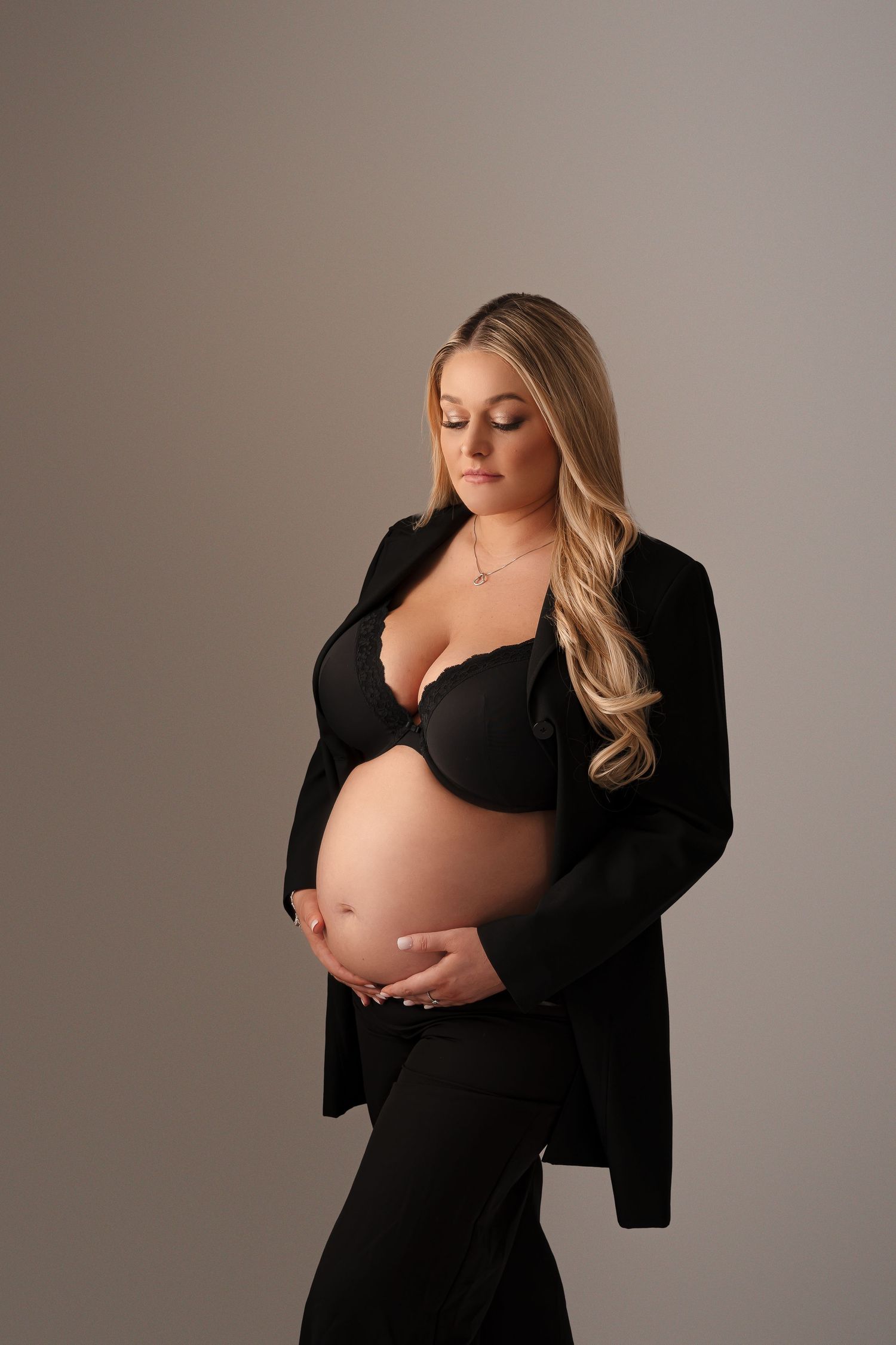 Stylish maternity photo of an expectant mother in black clothing against a beige background.