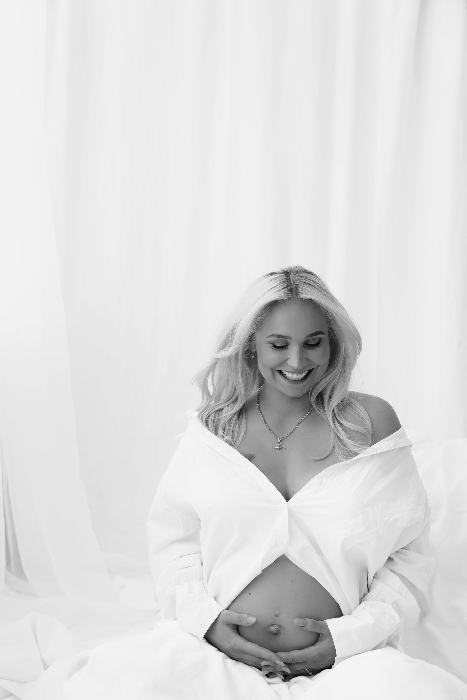 Artistic black and white maternity photo showing an expectant mother in white shirt cradling her belly.