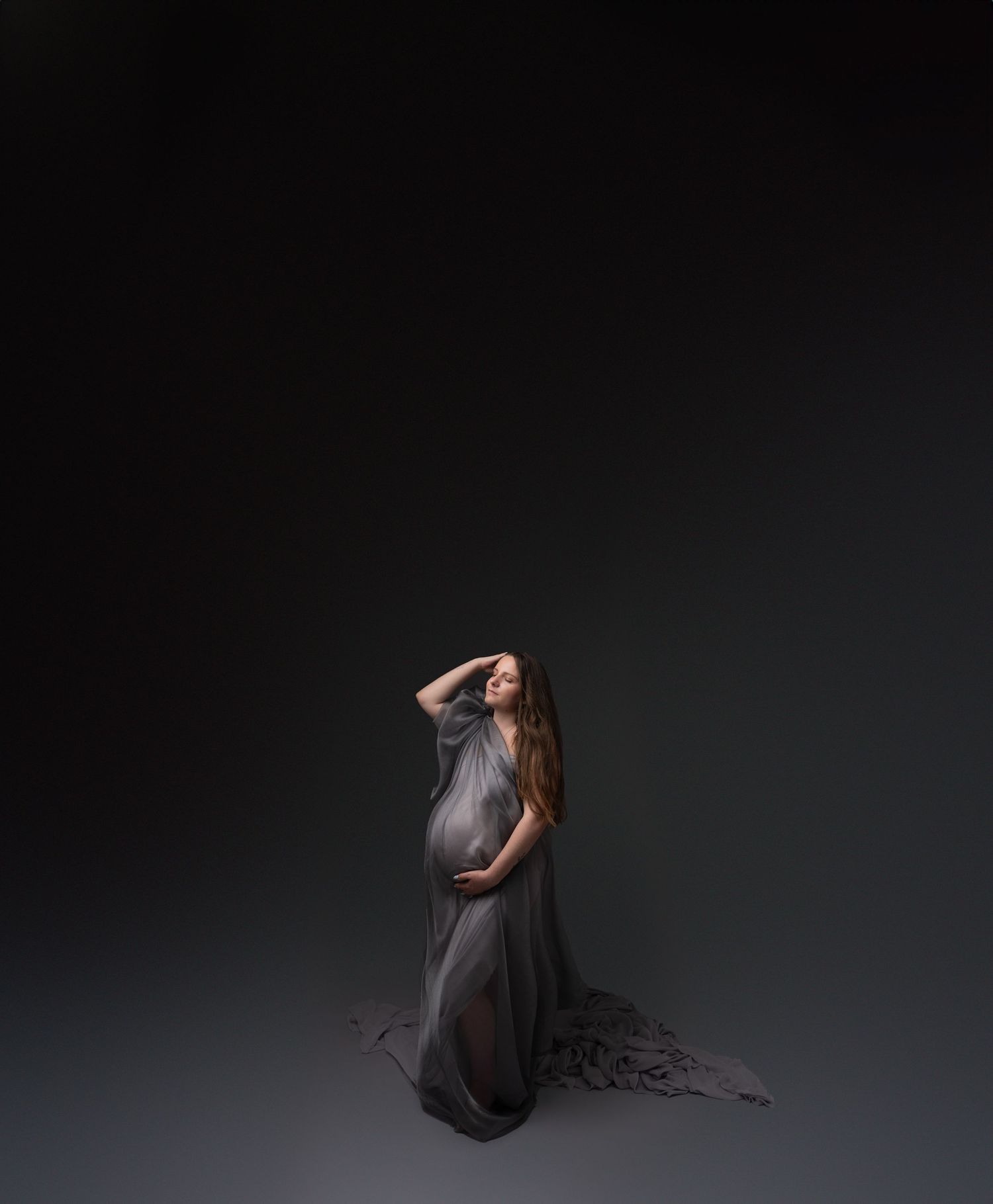 Moody maternity portraits with dramatic lighting and flowing dark fabric.