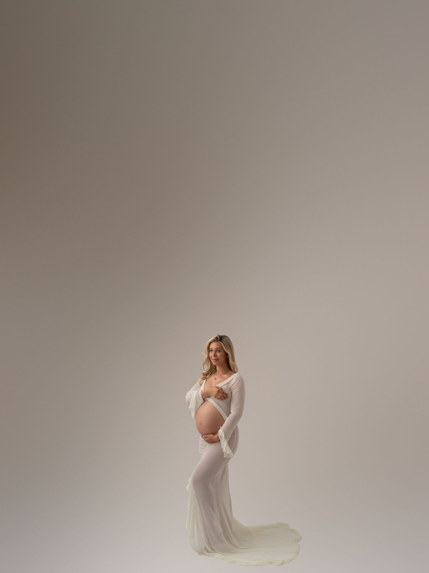 Elegant maternity portraits featuring flowing white dress against neutral background.