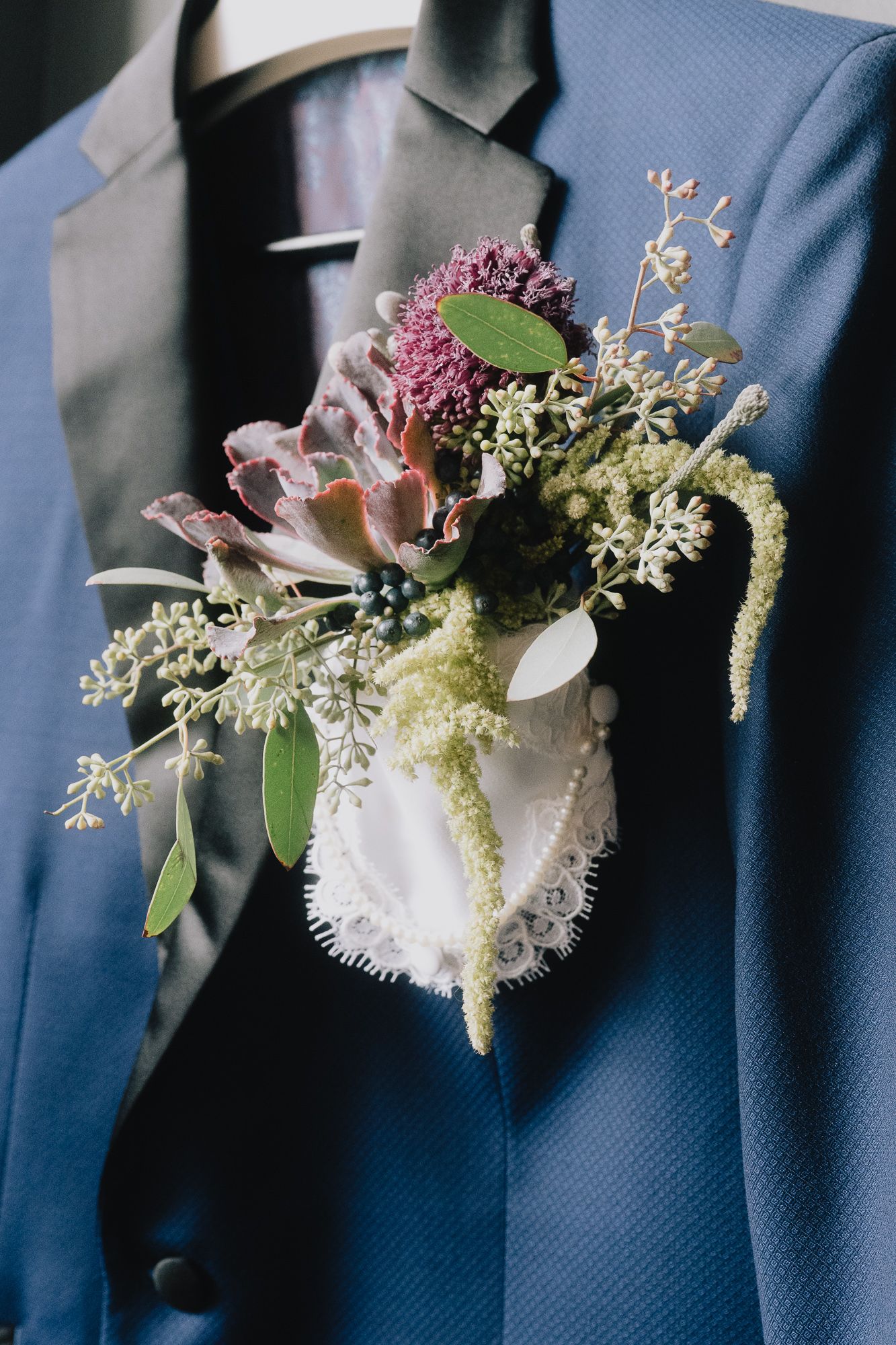 A delicate floral boutonniere with pink and white blooms pinned to a navy blue suit jacket.