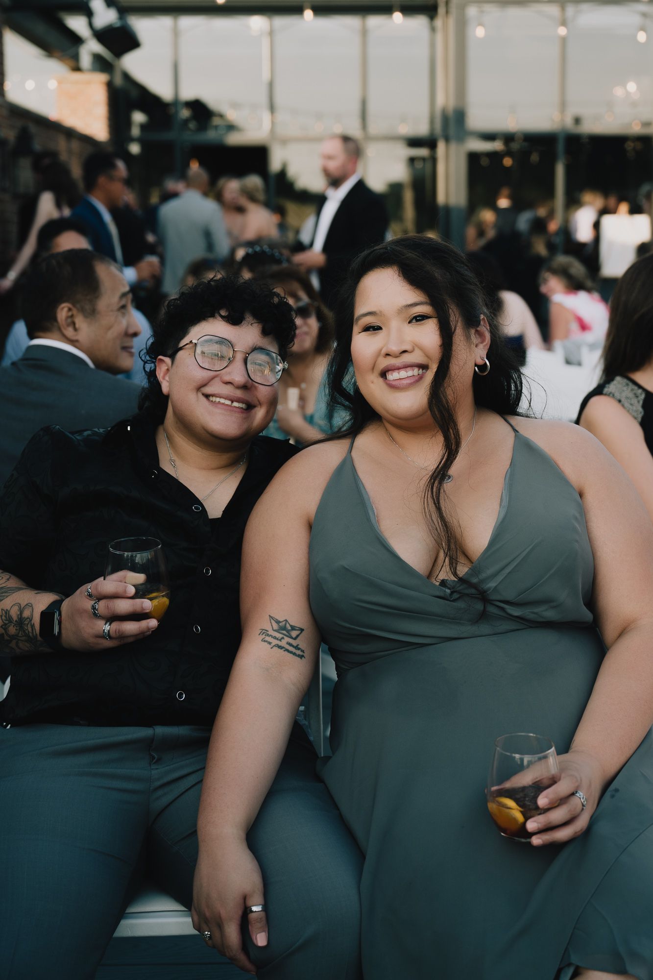 A queer couple sit close together at a wedding.