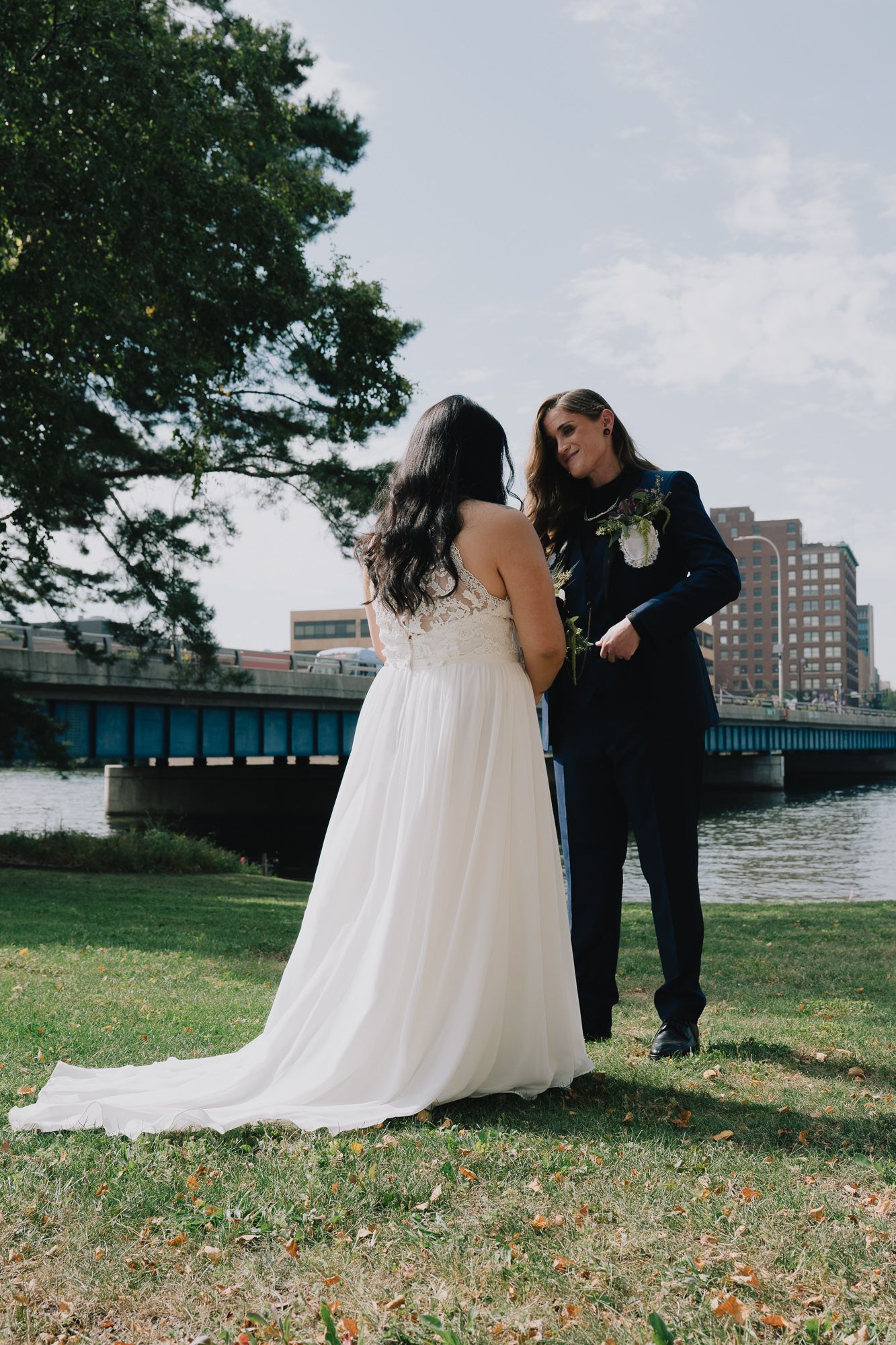 A joyful queer lesbian couple sharing a moment on their wedding day, with one in a white dress and the other in a navy suit.