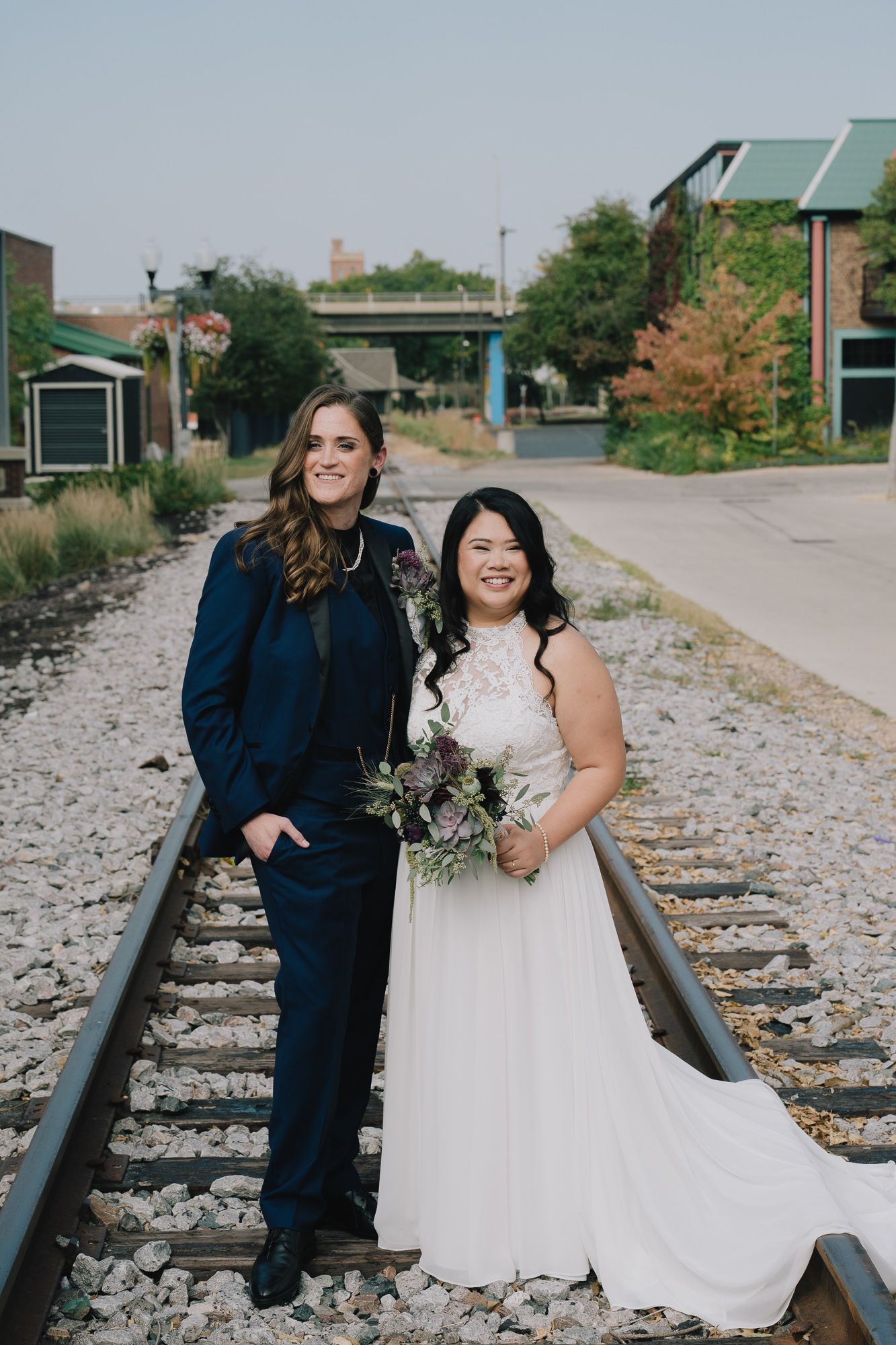 A queer lesbian couple poses romantically along railroad tracks in an intimate outdoor photo session.