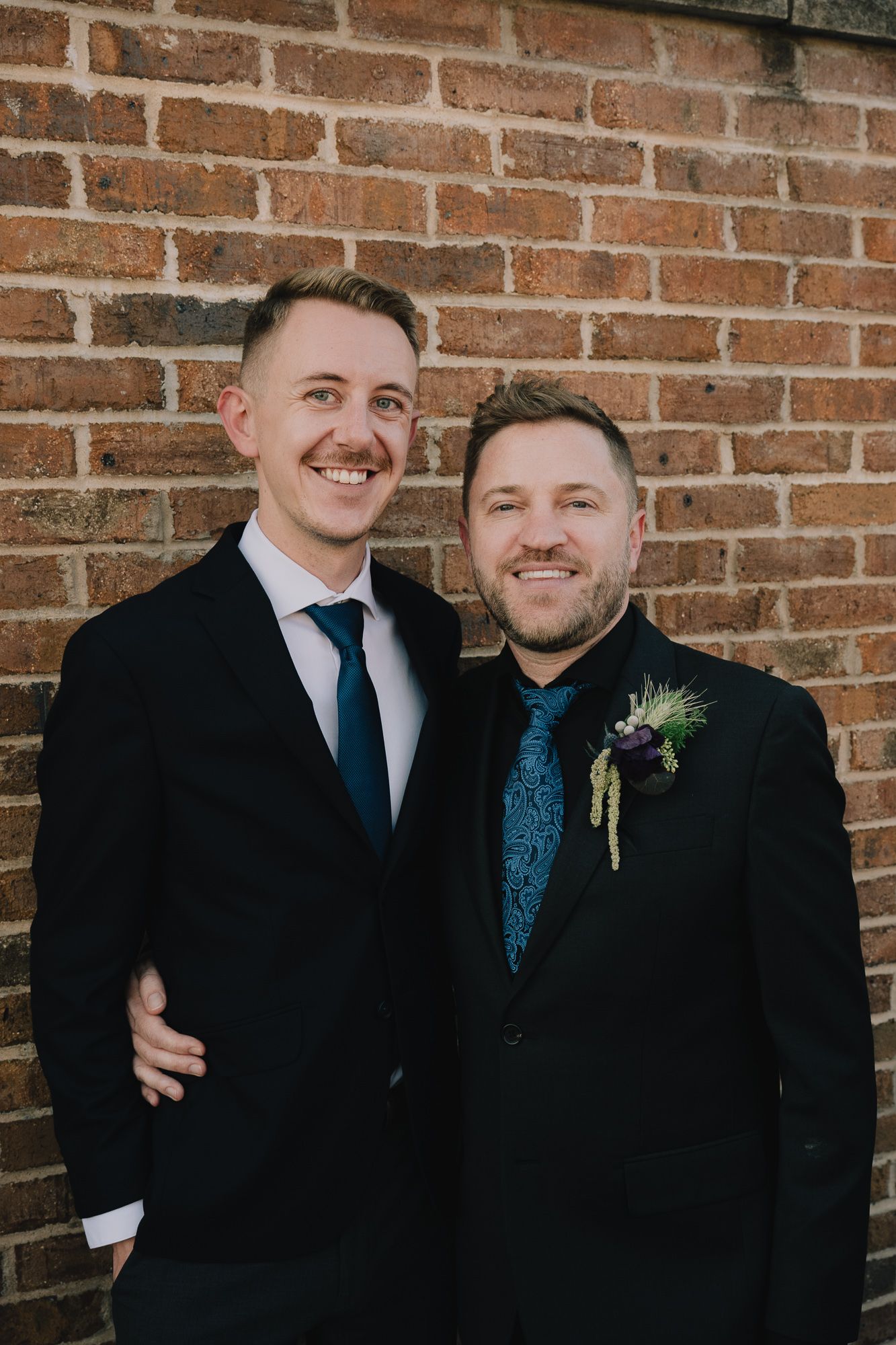 A queer gay couple pose next to one another for a photo.