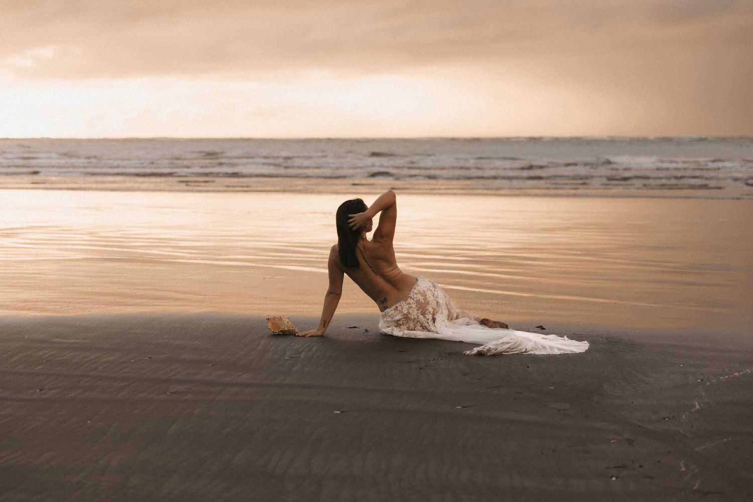 Dreamy beach portrait with warm sunset colors and flowing white dress.