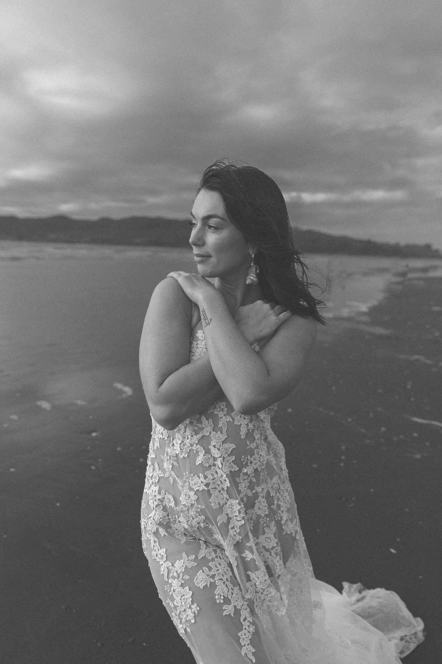 Black and white beach portrait with dramatic clouds and coastline in background.