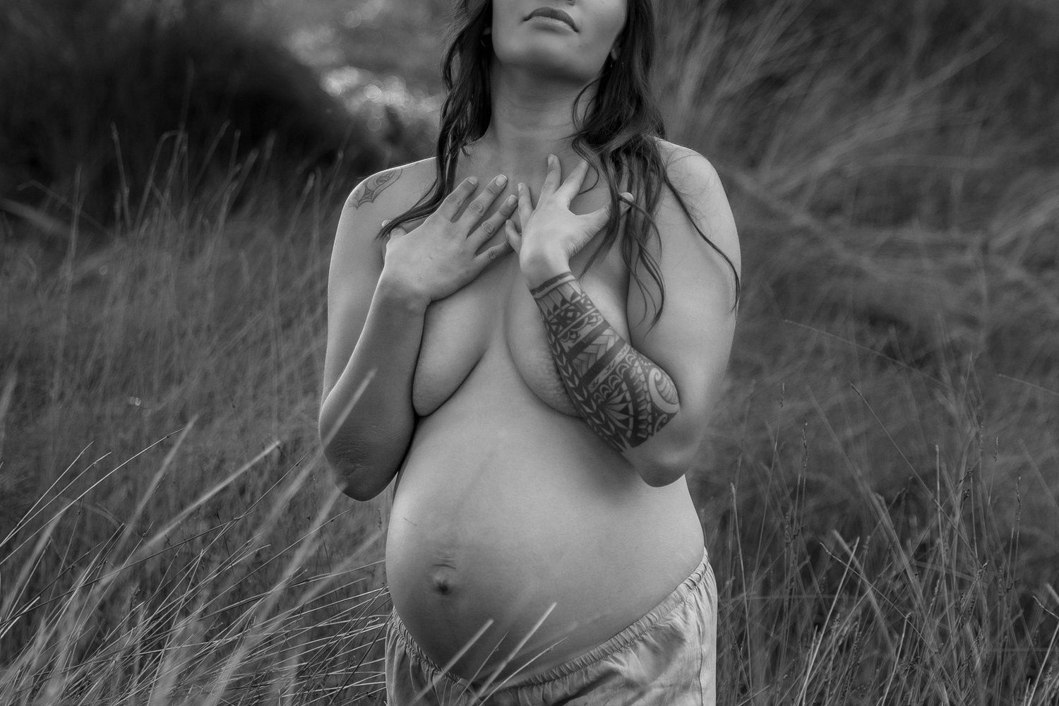 Intimate black and white maternity portrait in natural grassland setting.