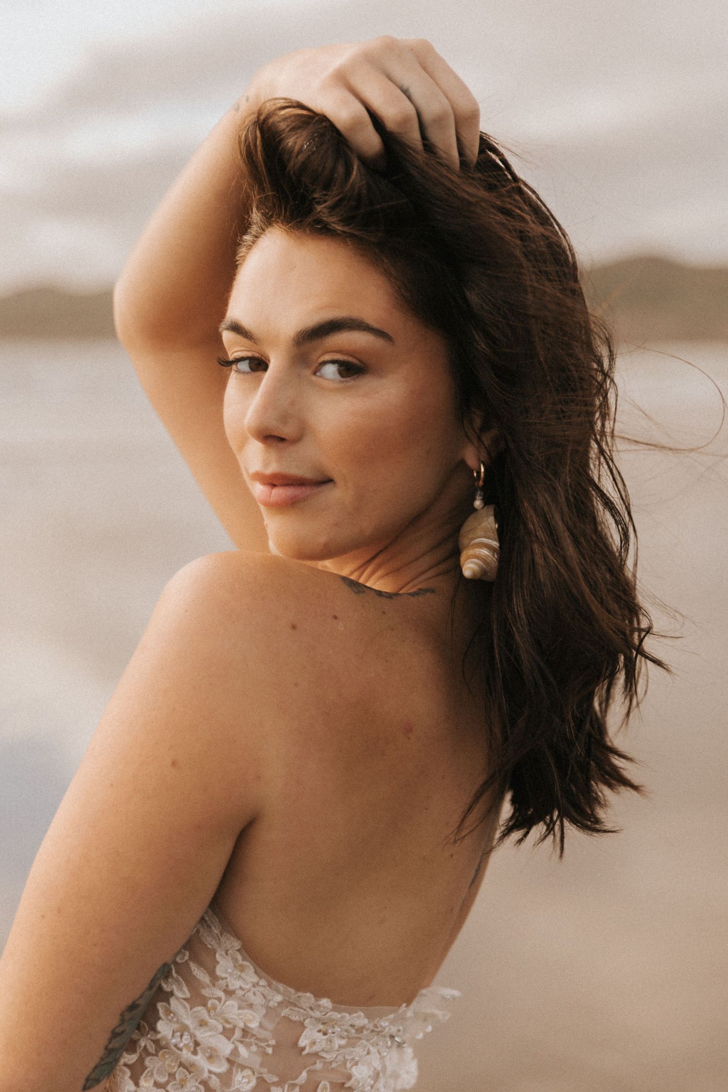 Artistic portrait on a beach with flowing white lace dress and natural lighting at sunset.