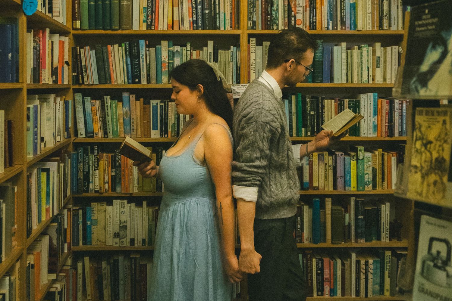 People browsing books in a cozy used bookstore with tall wooden shelves filled with various titles.
