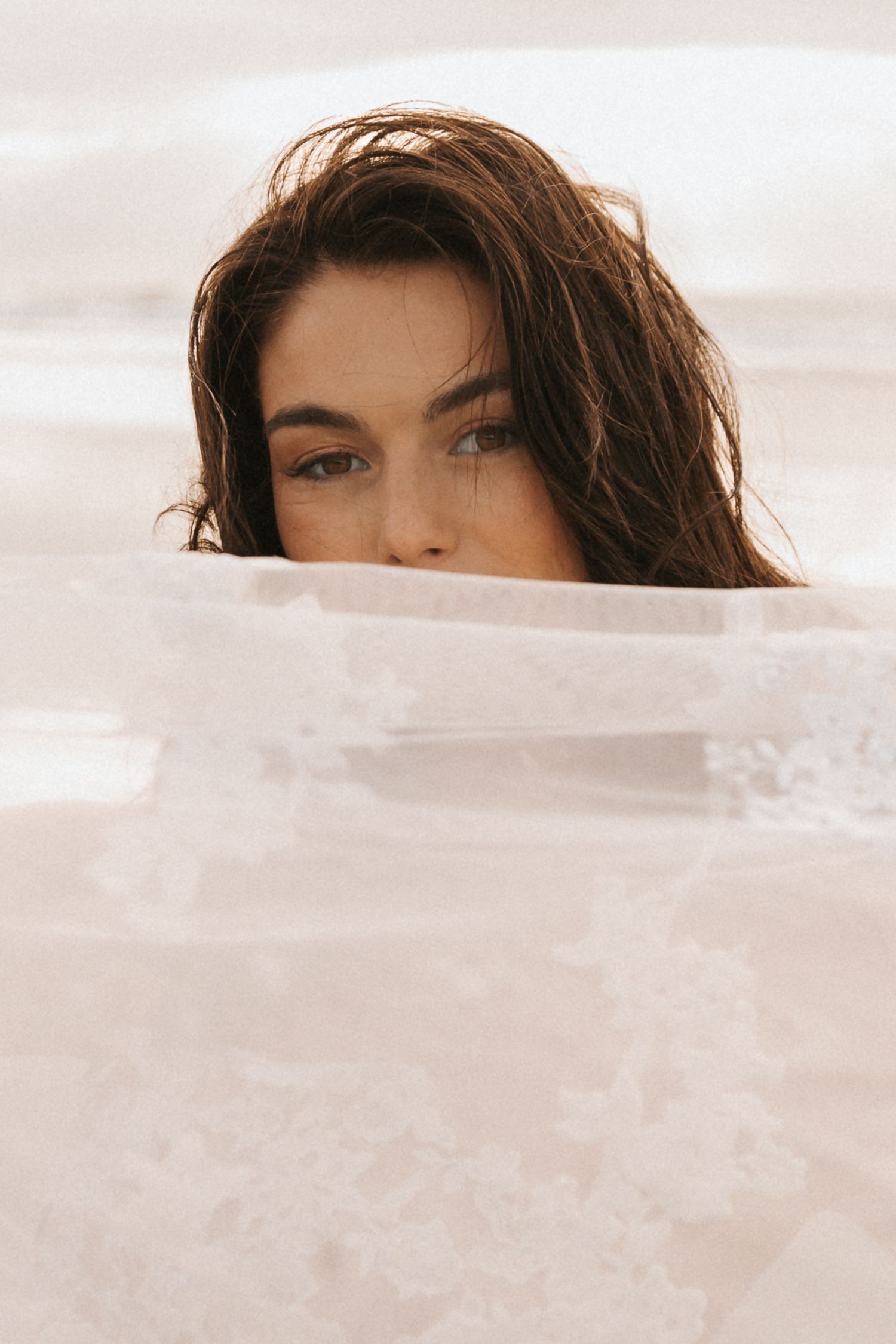 Artistic beach portrait with delicate white fabric creating a dreamy atmosphere.