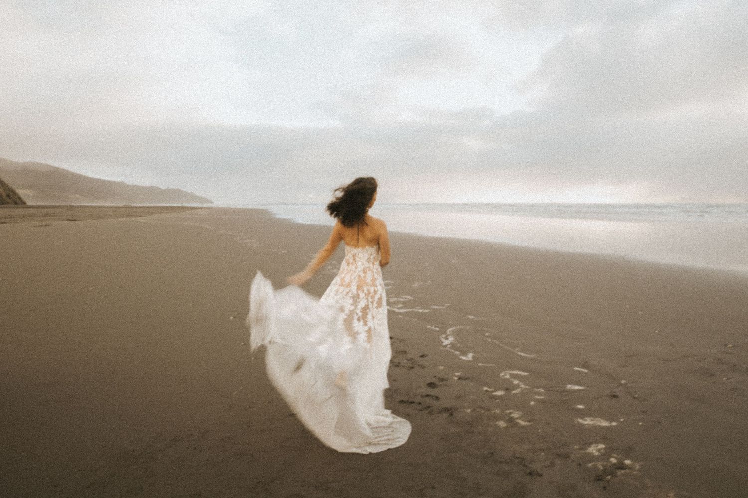 A flowing white dress billows in the wind on a misty beach at sunset.