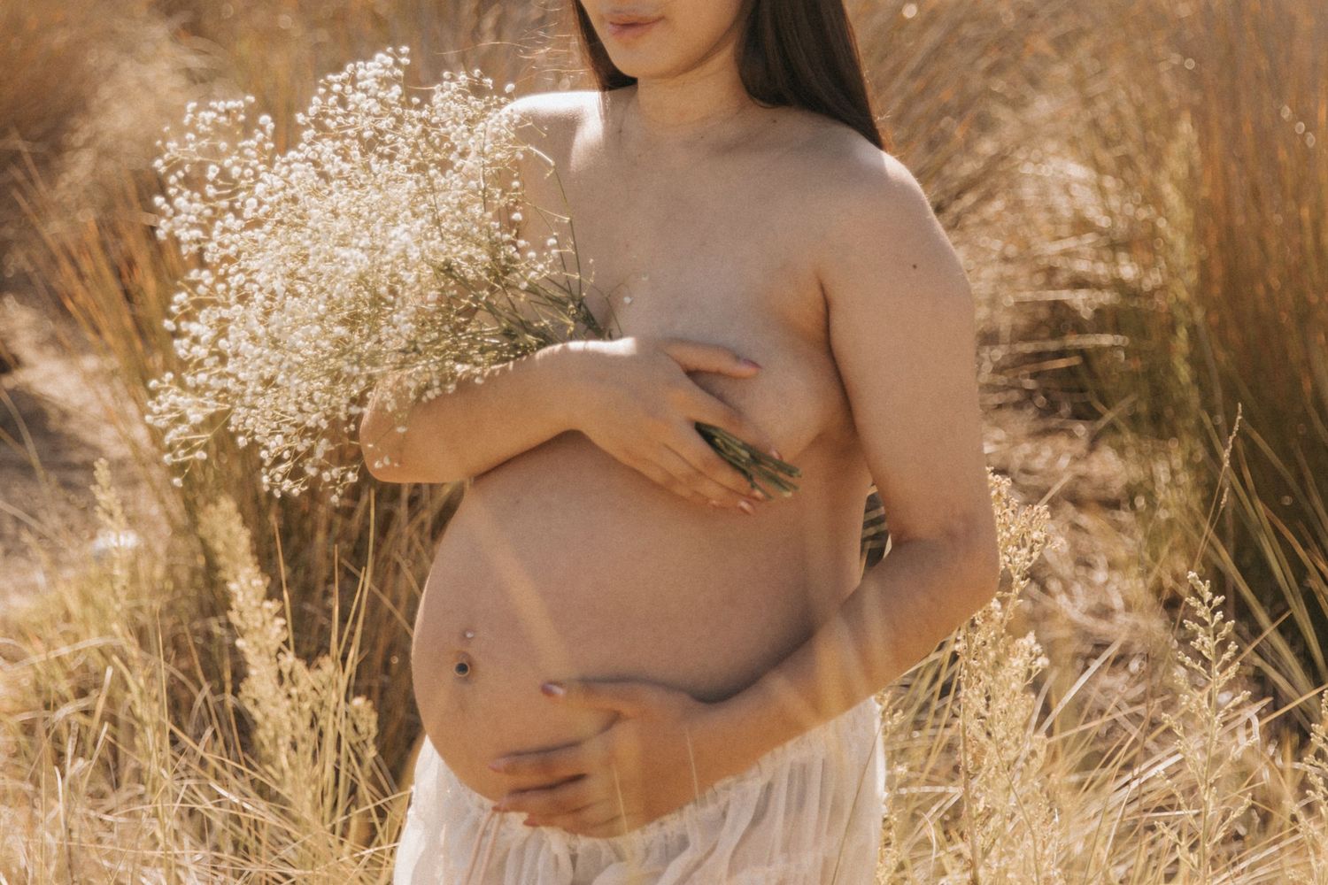 Intimate maternity portraits with baby's breath flowers in natural outdoor setting.