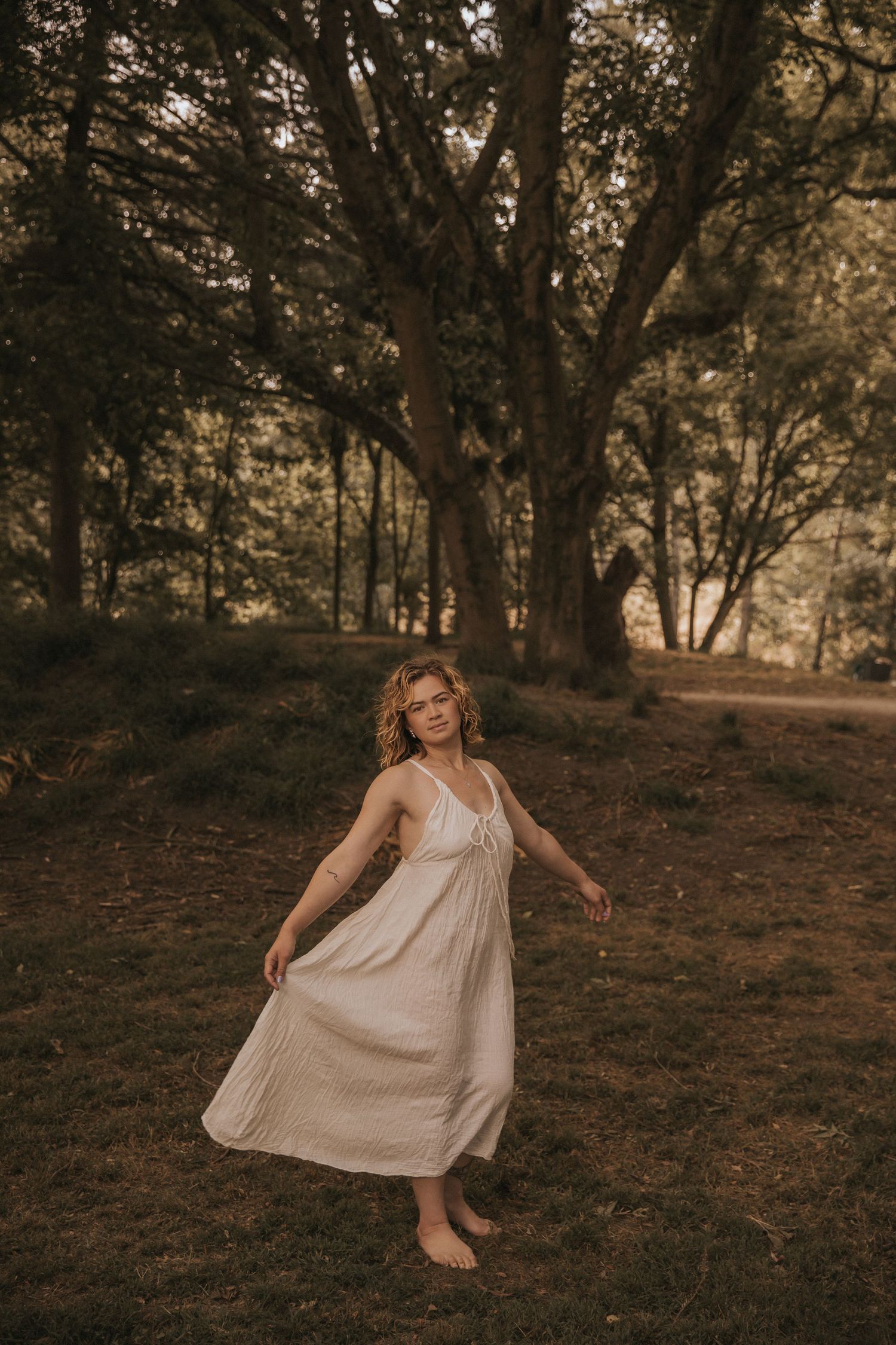 A flowing white dress twirls in motion during a forest photoshoot at golden hour.
