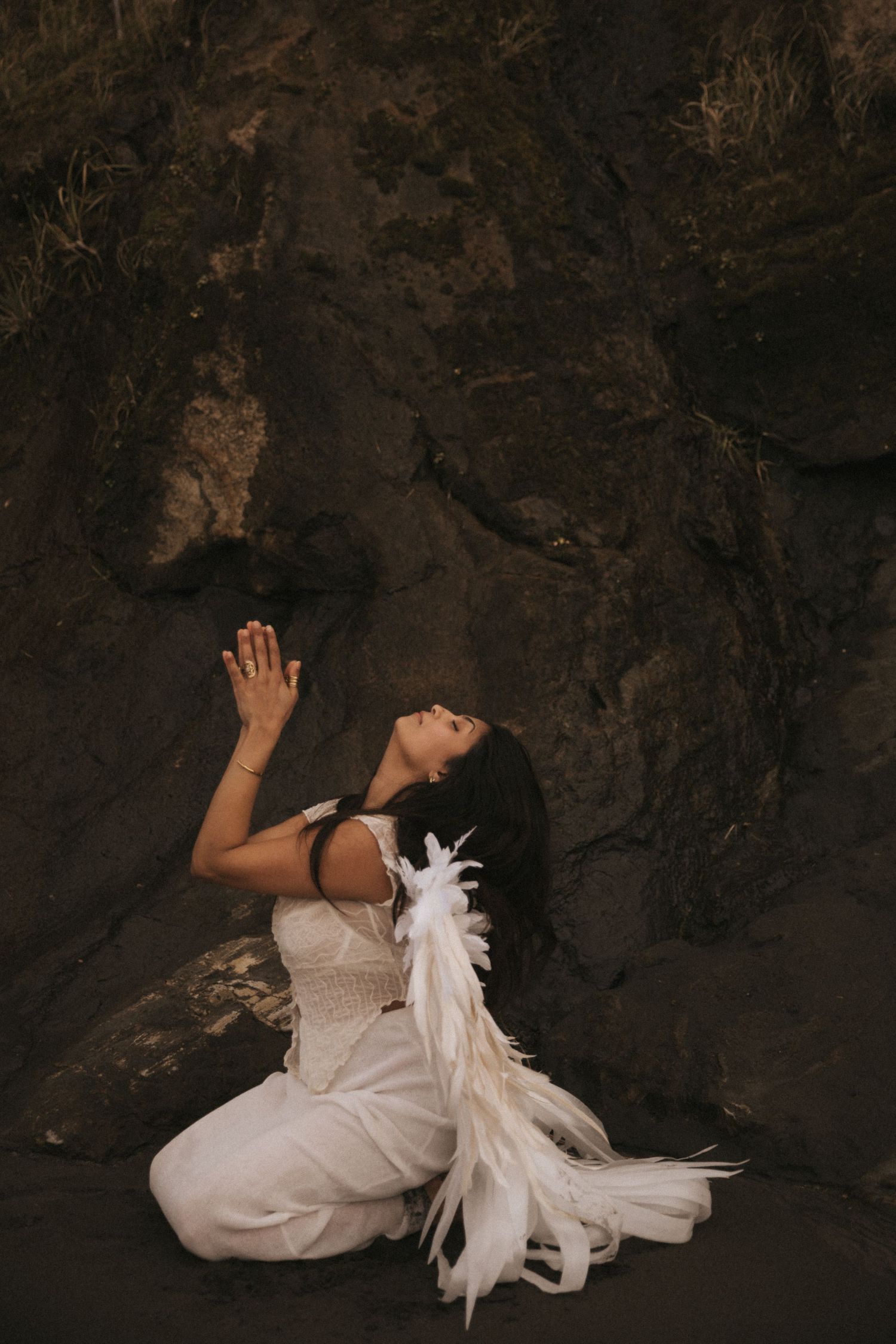 A figure in a flowing white dress performs an artistic dance movement against a dark rocky cave backdrop.