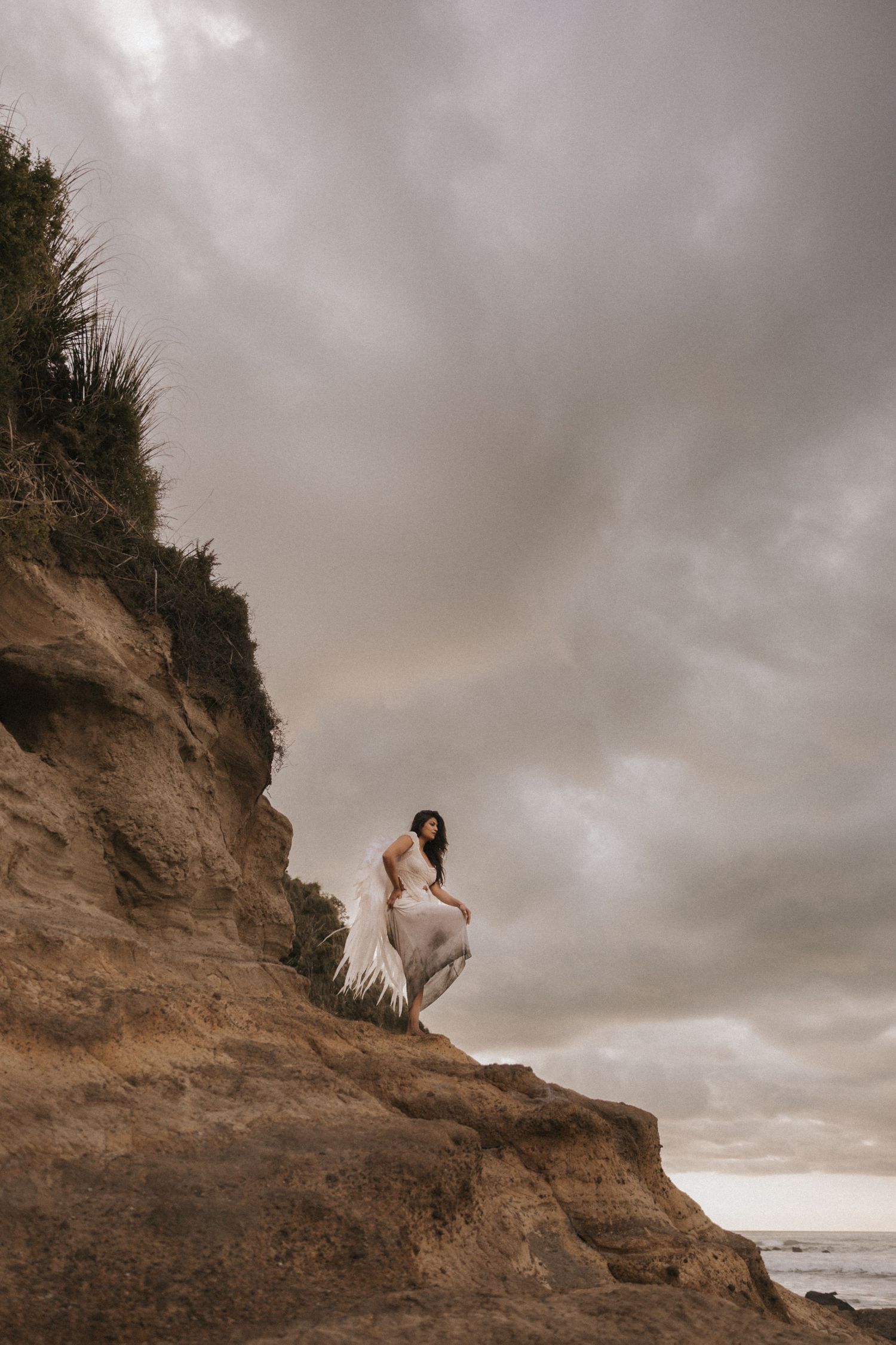 A romantic coastal scene with a couple embracing on a dramatic cliff edge under moody storm clouds at sunset.