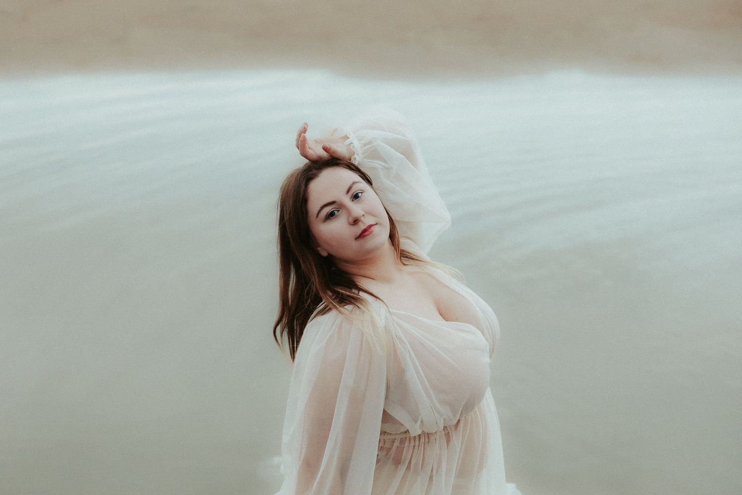 Romantic beach photoshoot featuring flowing cream-colored dress in soft lighting.