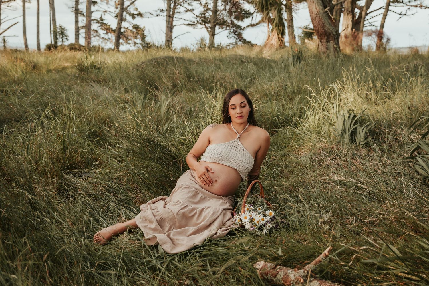 Natural maternity photography in a forest setting with sunlight filtering through pine trees.