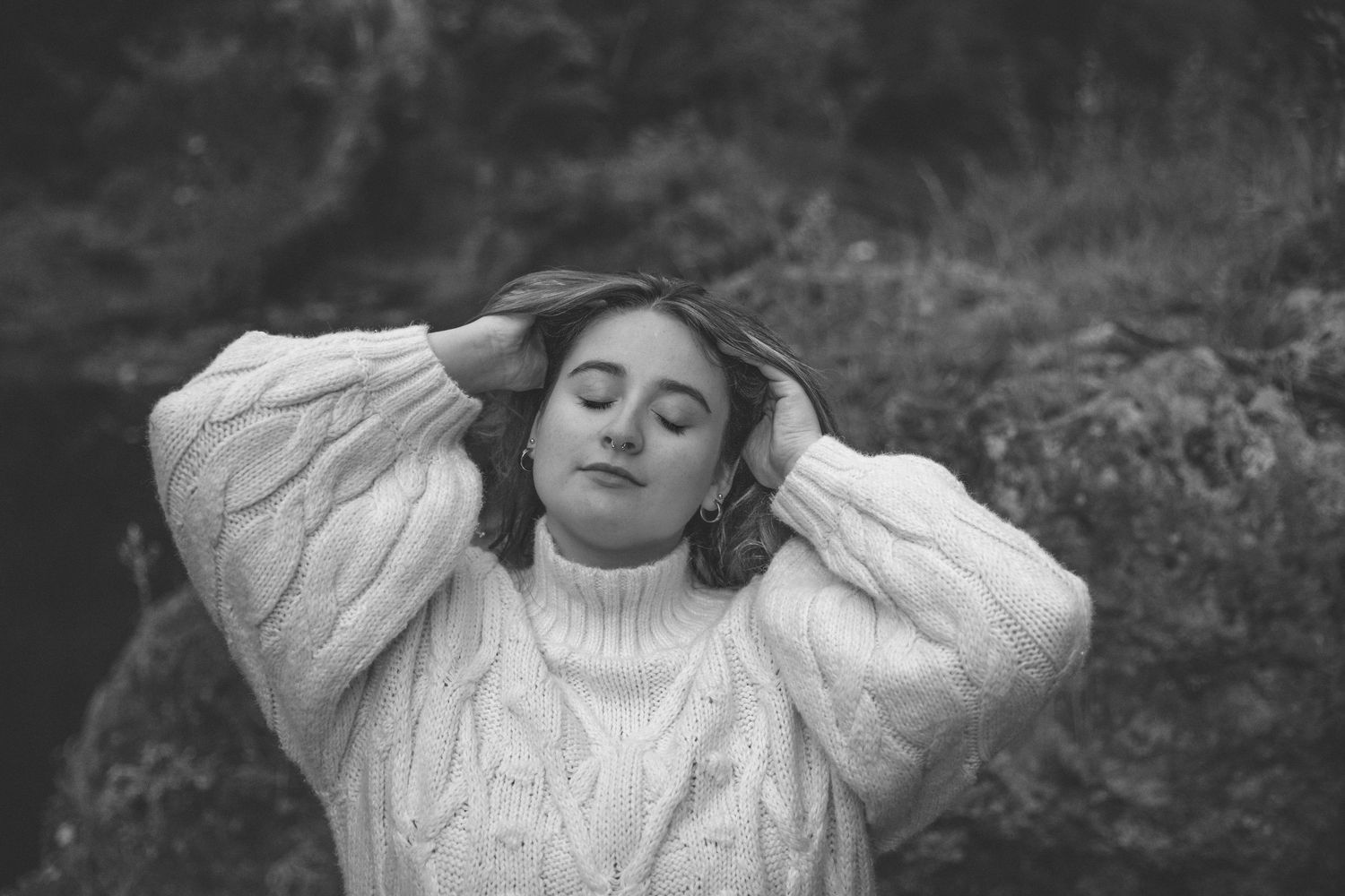 A black and white photo series showing a beautiful woman posing in a cream sweater against a dark background.