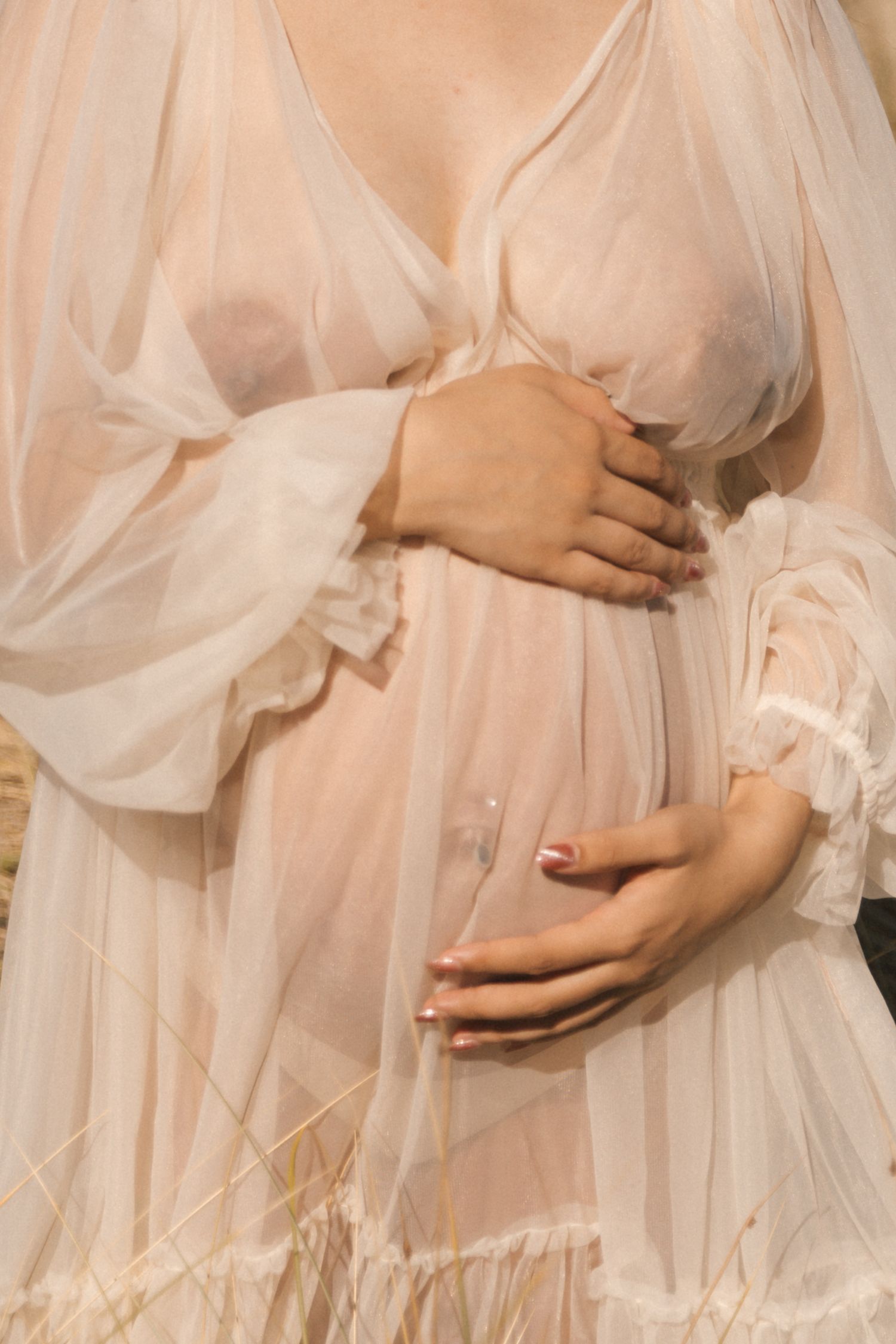 Close-up details of flowing sheer fabric draping over a pregnant belly.