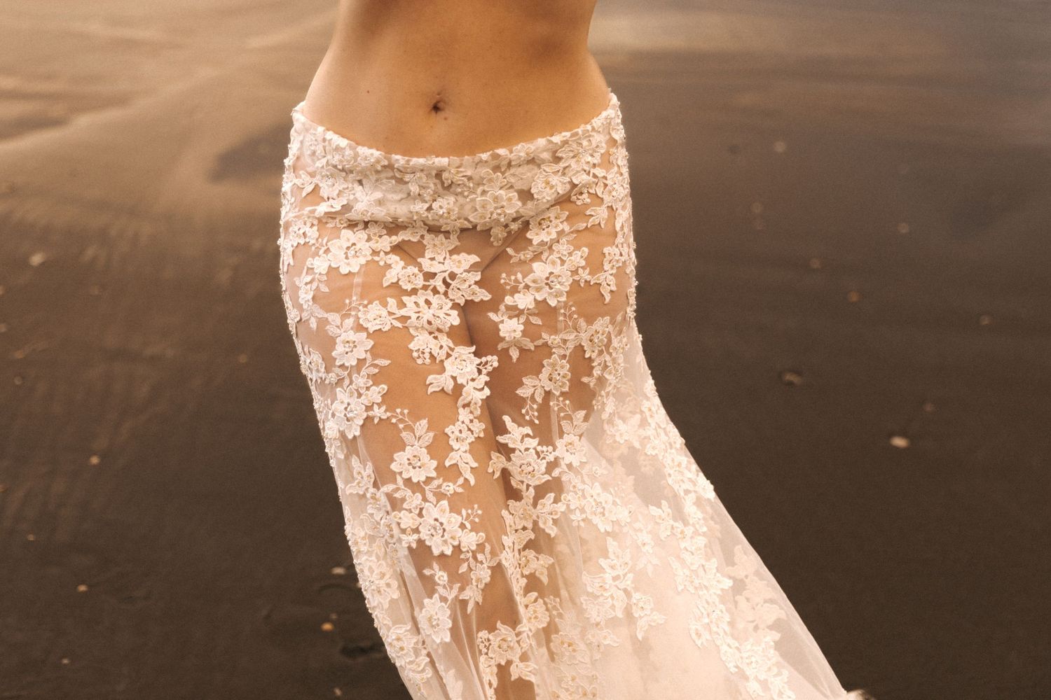 A figure in a flowing white dress poses dramatically on a misty beach at sunset.