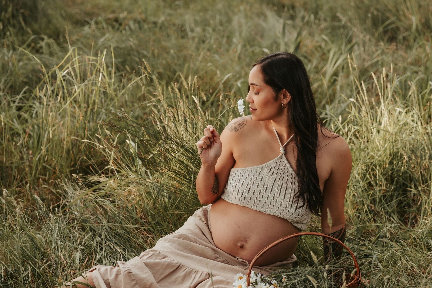 Maternity photos taken in tall grass showing a woman in a beige dress laying on her side.