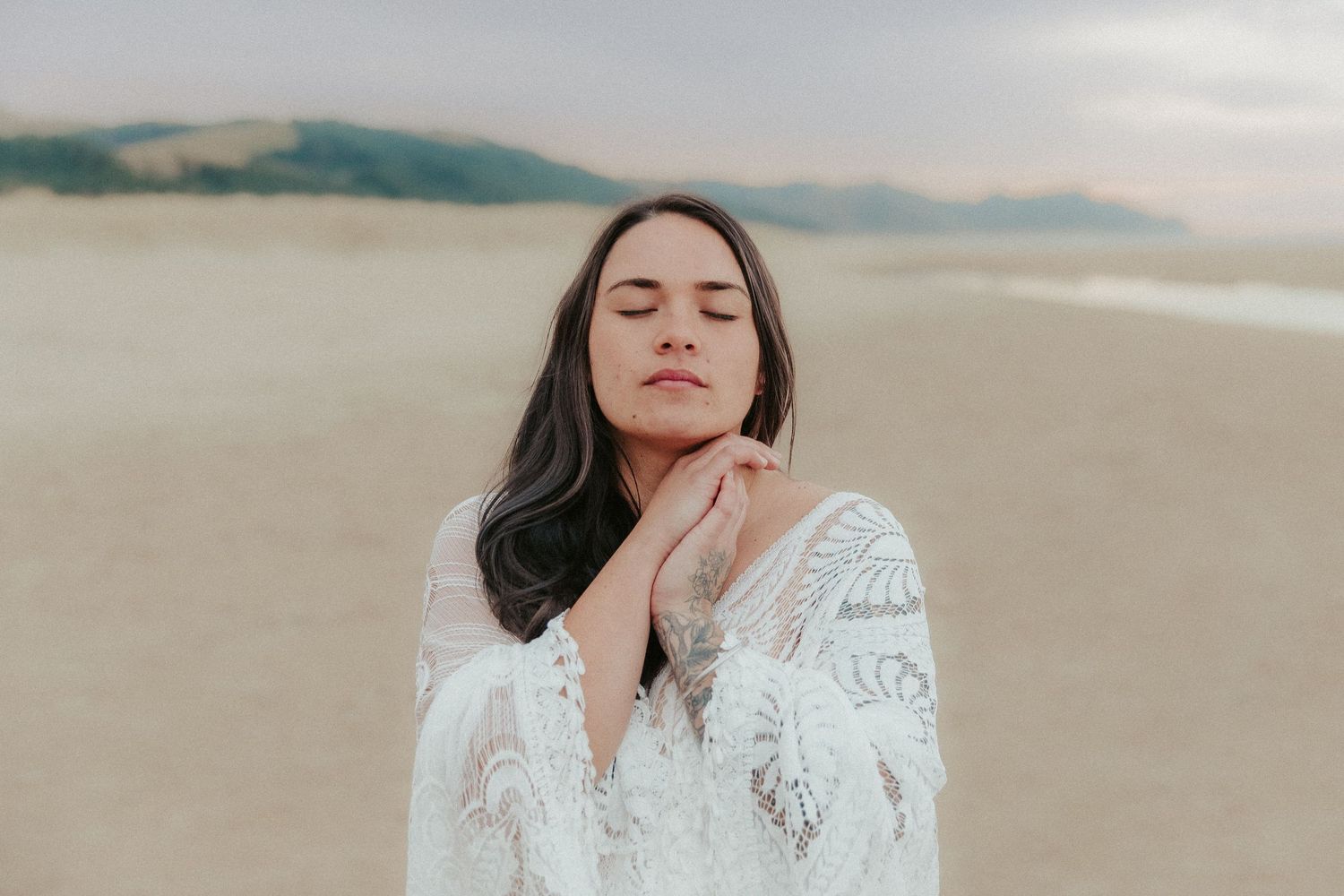 Ethereal beach photoshoot featuring a white lace dress against a misty coastal backdrop.