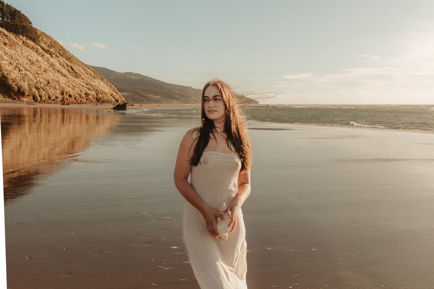 Scenic beach maternity photoshoot with golden sunlight and coastal cliffs in the background.
